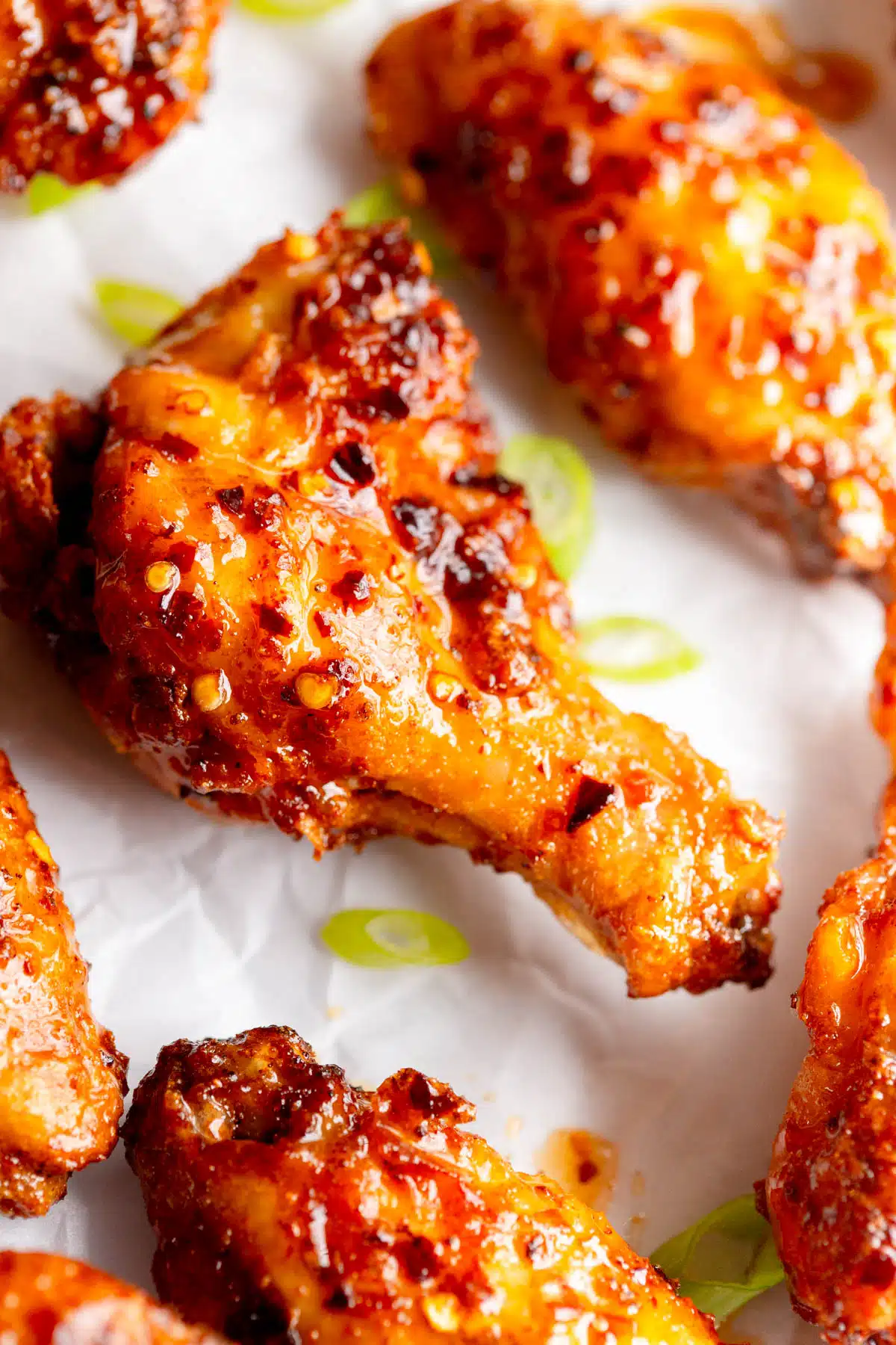 Hot Honey Wings on parchment paper with chopped green onions scattered around it. 