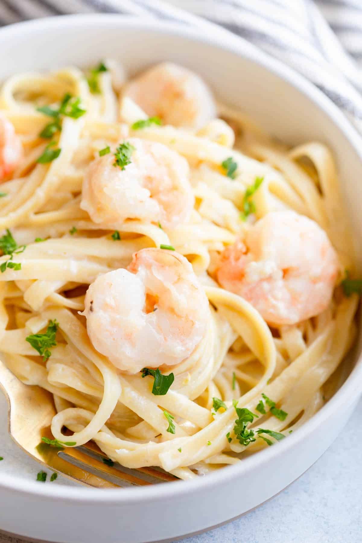 Creamy Lemon Shrimp Pasta in a shallow pasta bowl, topped with fresh parsley and a gold fork next to it.