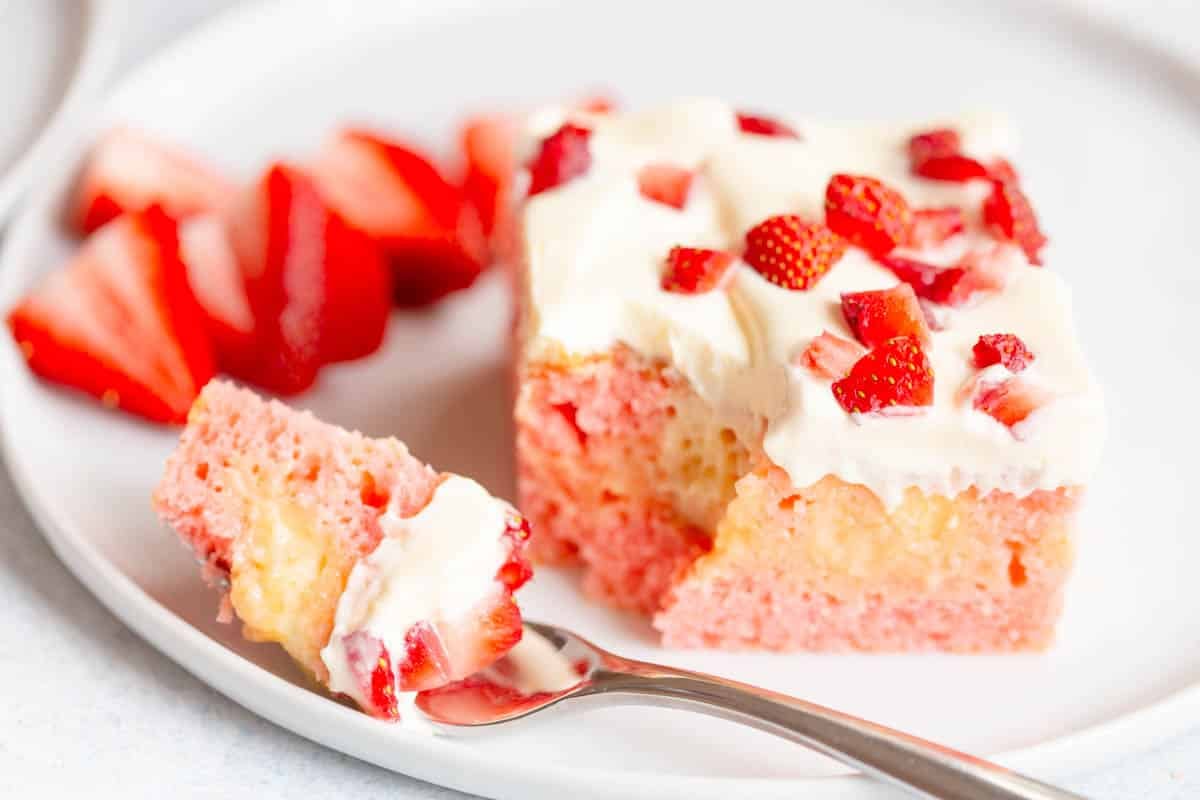 A slice of Strawberry Pudding Poke Cake on a white plate, with a bite taken out of it with a silver fork.