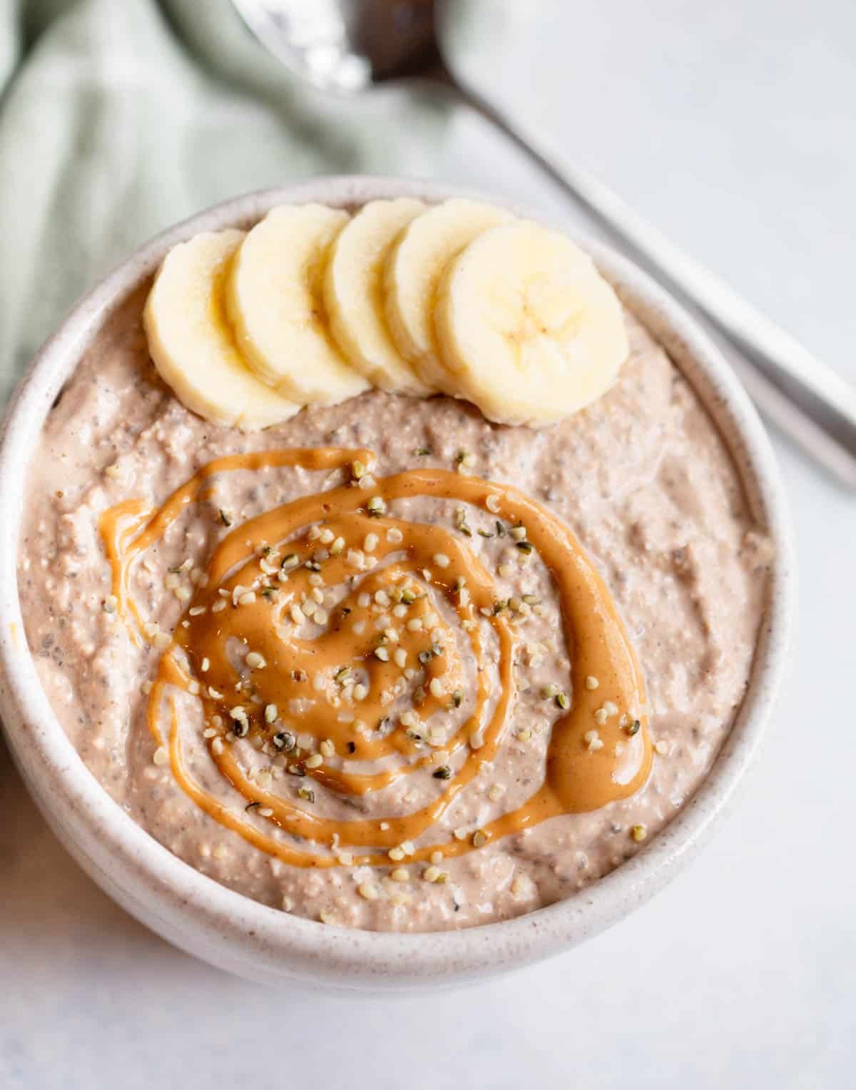 Peanut Butter Chocolate Blended Overnight Oats in a speckled bowl topped with sliced bananas, a drizzle of peanut butter, and hemp seed hearts. 