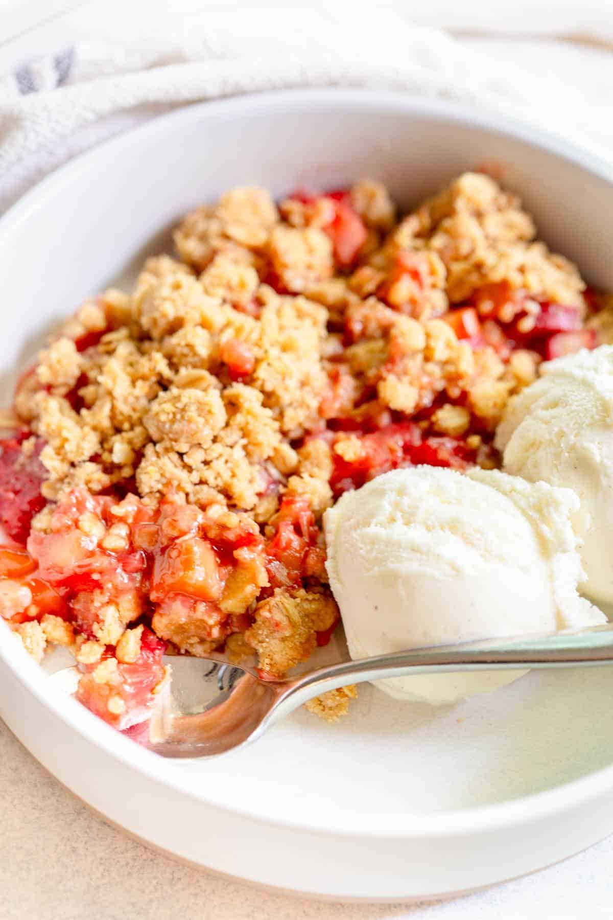 Strawberry Rhubarb Crisp in a shallow bowl with two scoops of vanilla ice cream 