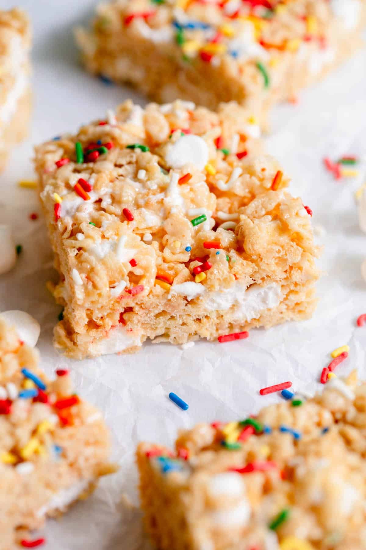 Birthday Cake Rice Krispie Treat on a piece of parchment paper with sprinkles scattered around it. 