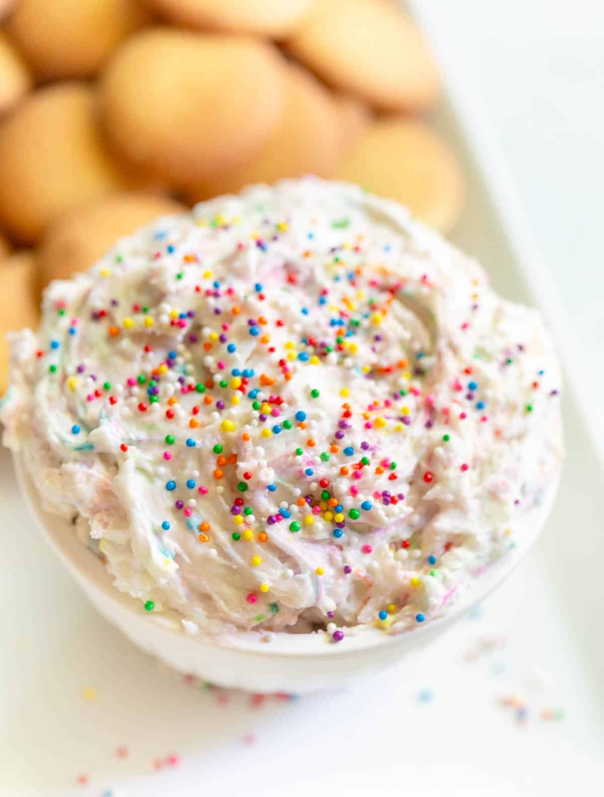 Dunkoaroo dip in a white bowl topped with sprinkles and vanilla wafers in the background.