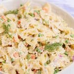 Tuna Pasta Salad in a white bowl with a blue and white striped towel and silver spoon in the background.