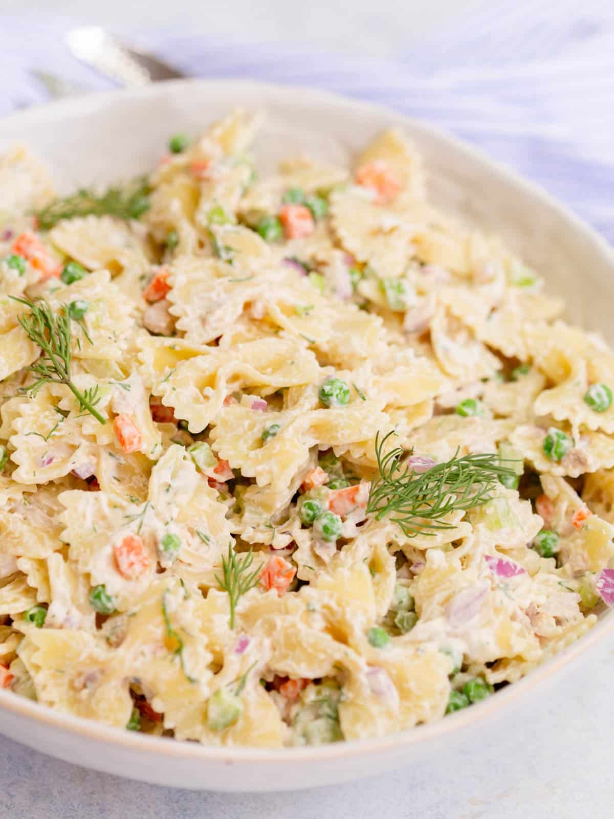 Tuna Pasta Salad in a white bowl with a blue and white striped towel and silver spoon in the background.