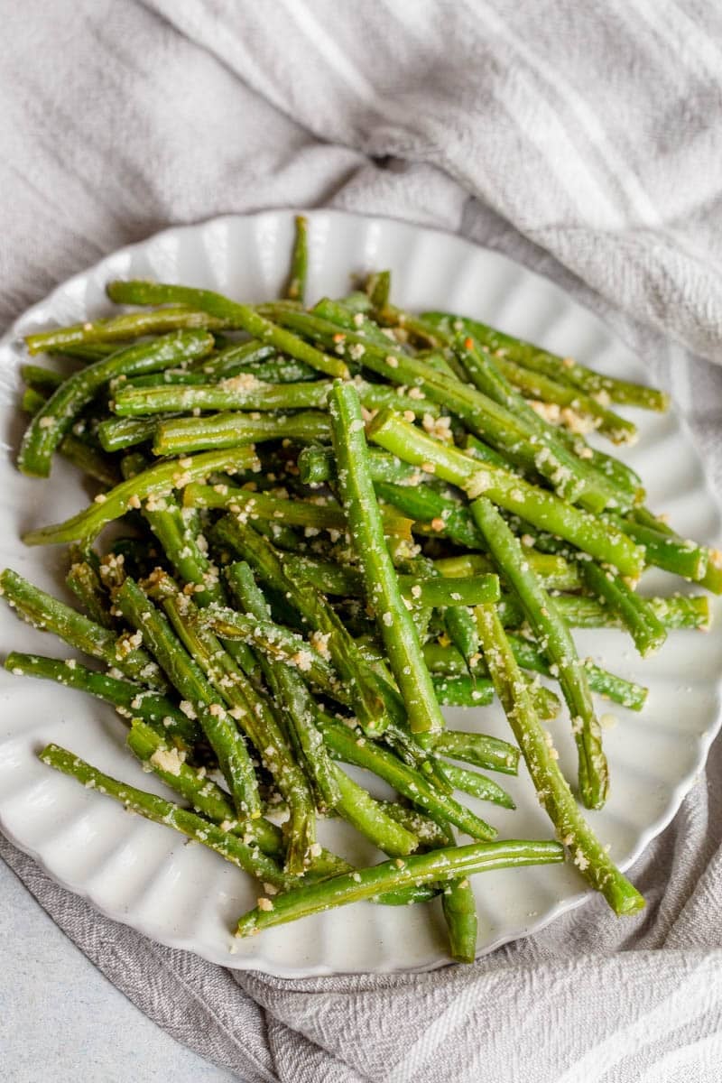 Garlic Parmesan Green Beans on a plate with scalloped edges and a napkin in the background. 