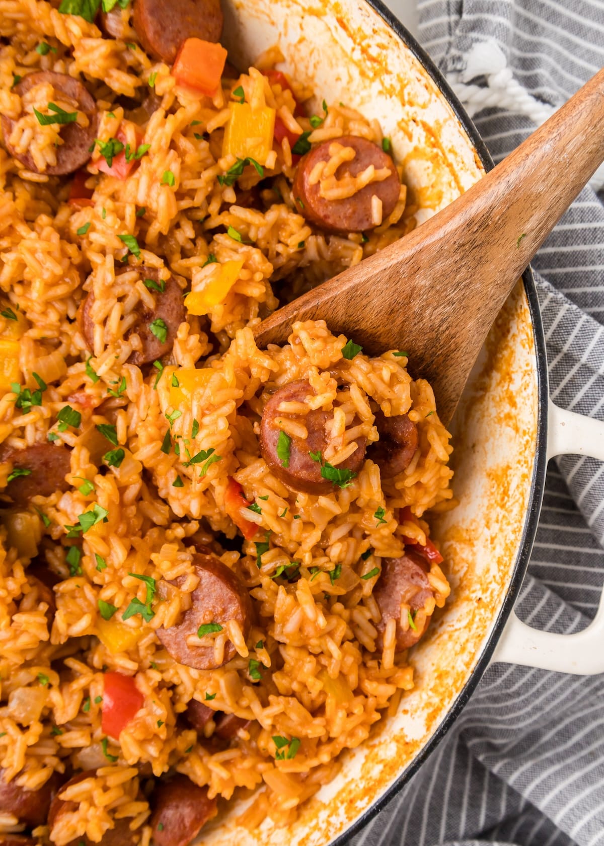 Cajun Sausage and Rice in a white skillet with a wooden spoon resting inside. 