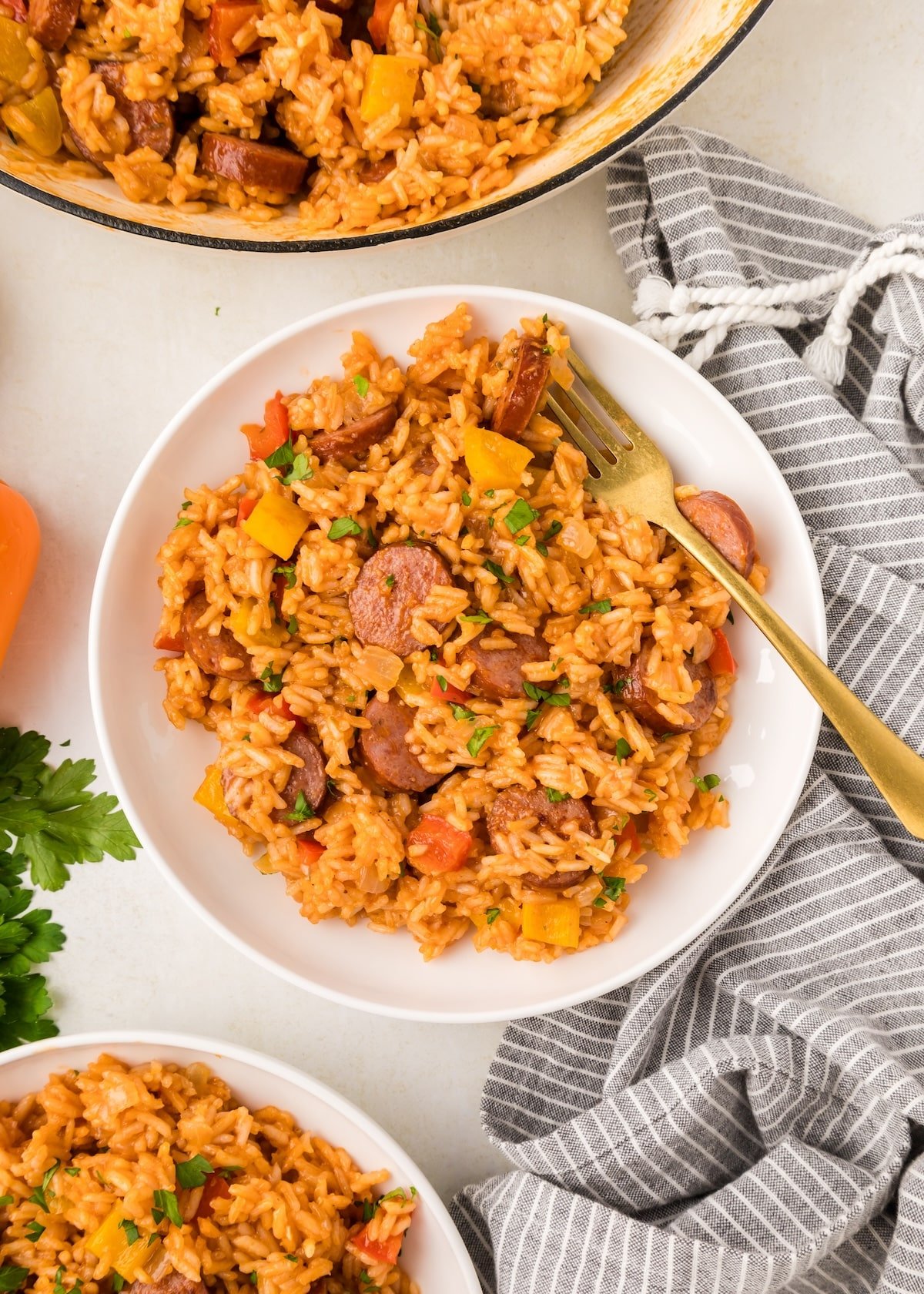 Cajun Sausage and Rice in a white serving bowl with a gold spoon resting inside. There's a gray striped napkin next to the bowl and fresh parsley sprinkled on top of the dish. 