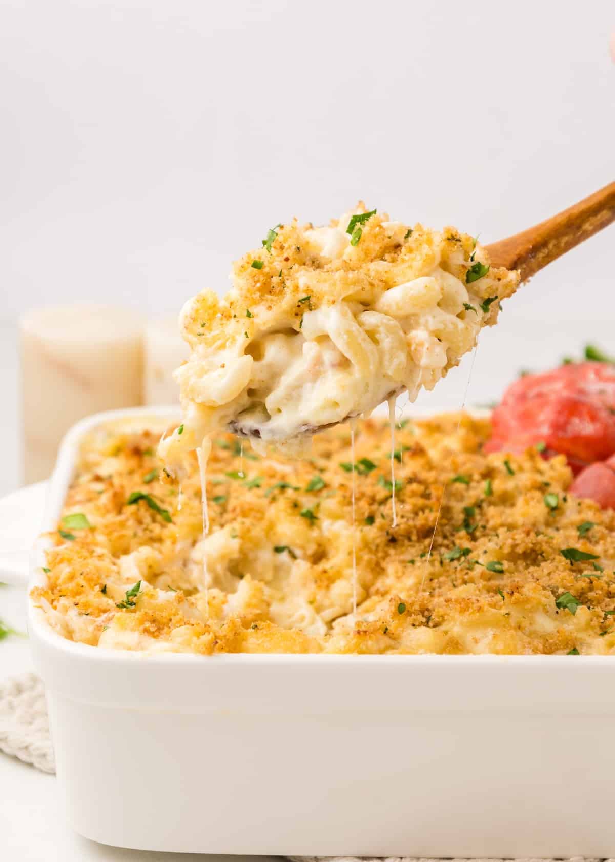 Lobster Macaroni and Cheese in a white baking dish with a spoonful lifted out of the pan. There are cheese pulls dripping from the spoonful. 