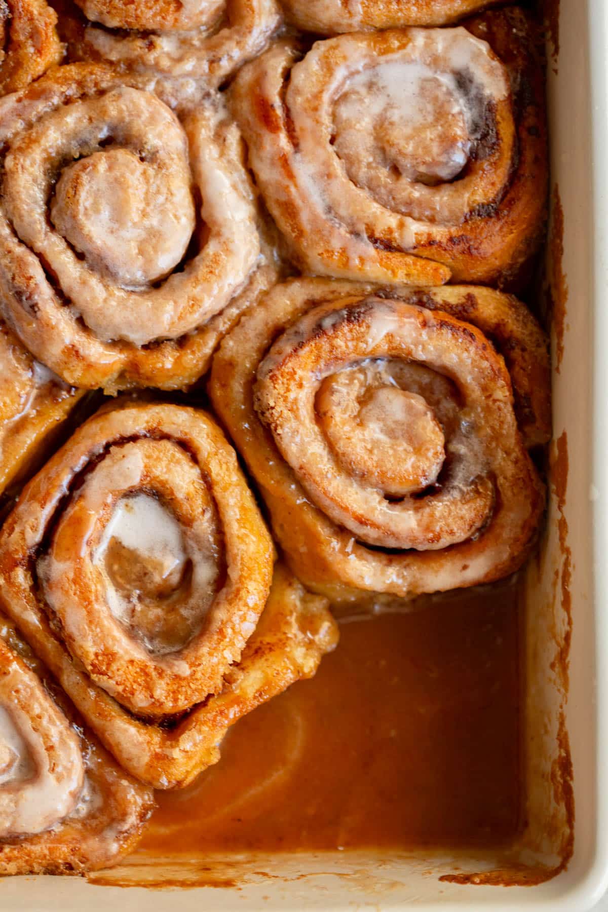 A white pan with pumpkin spice cinnamon rolls with one pumpkin taken out. 