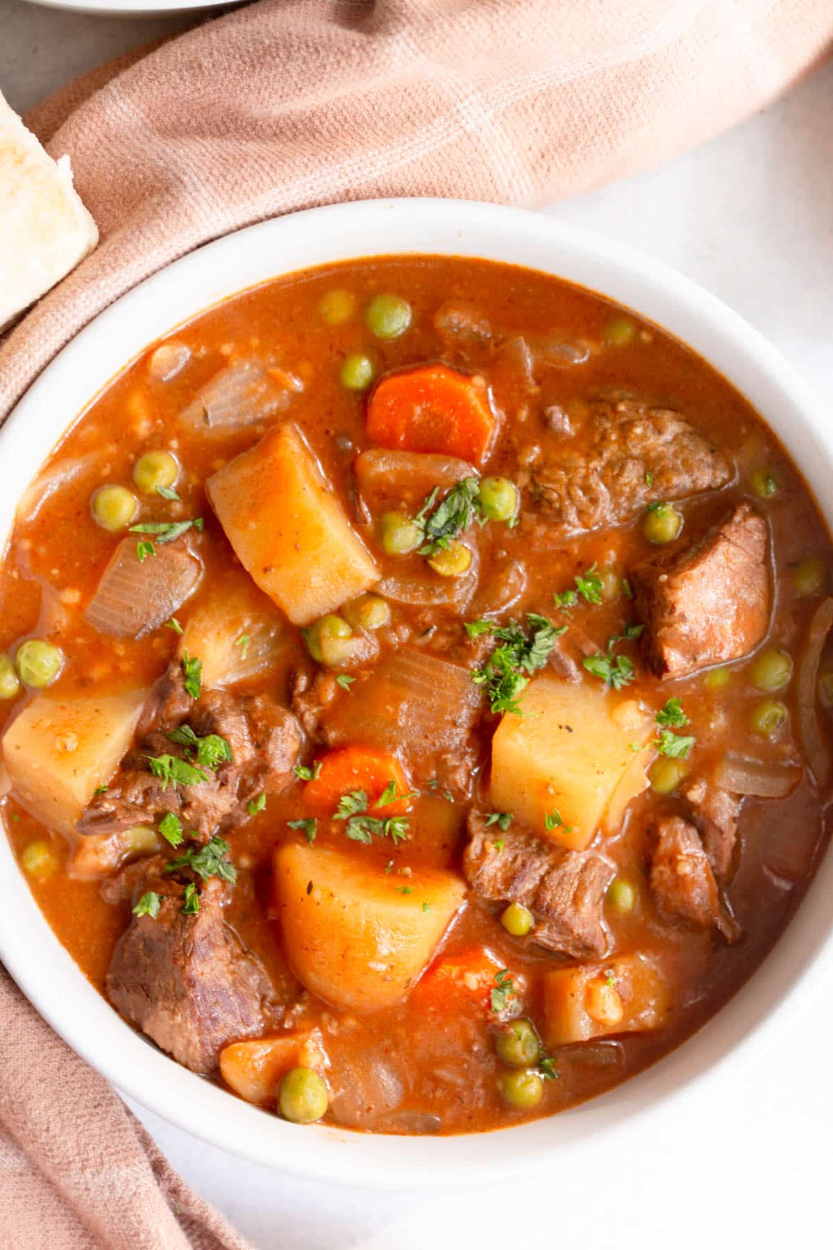 Slow Cooker Beef Stew in a large white bowl with a terra cotta colored towel around it. 