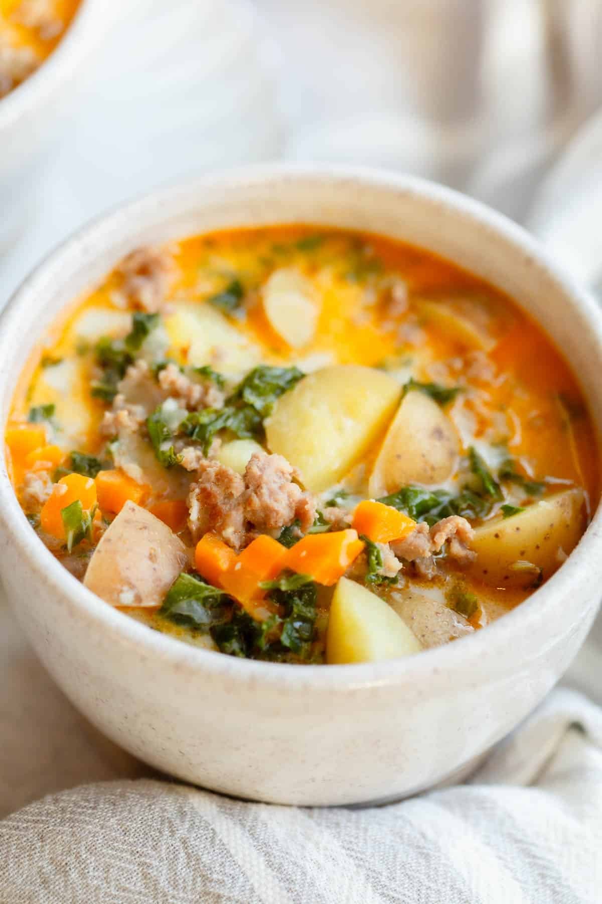 Sausage Kale Potato Soup in a cream speckled bowl with a cream colored towel in front of it. 