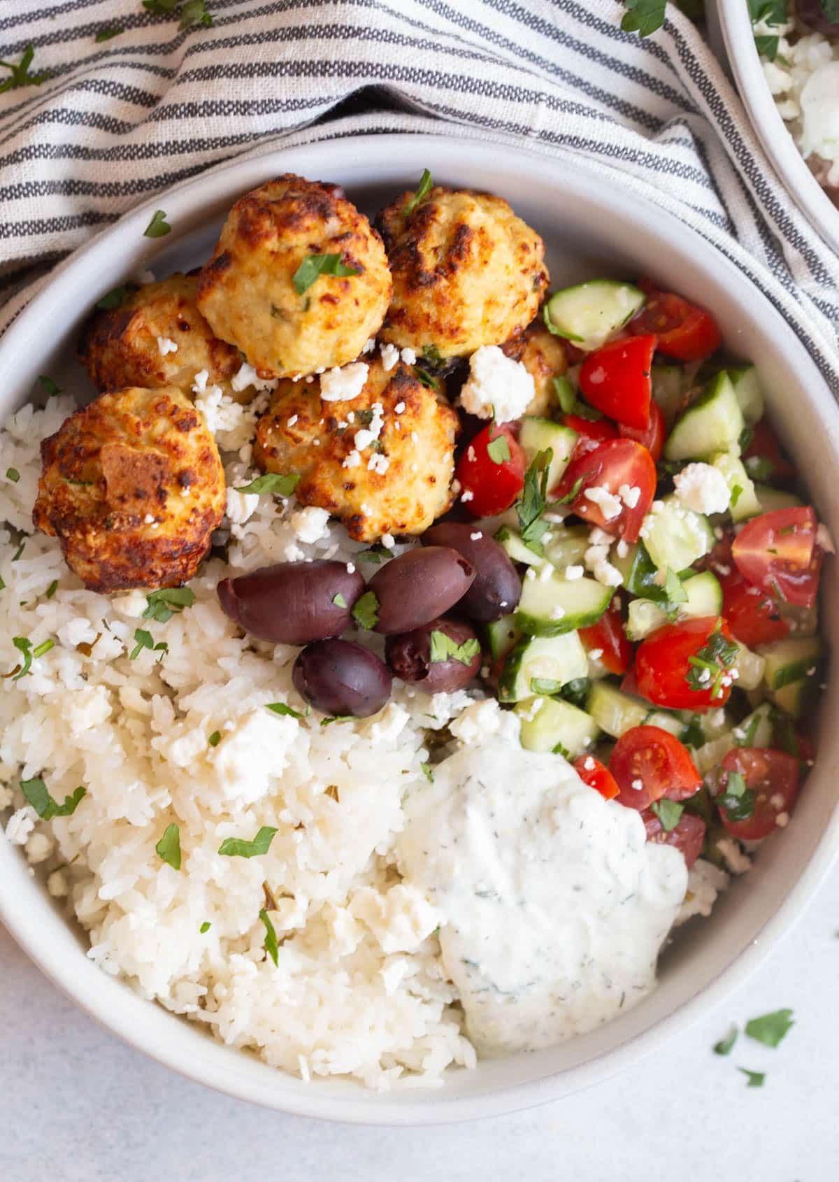 Greek Chicken Meatball Bowls in a shallow cream bowl with a gray background and a striped towel next to it. 