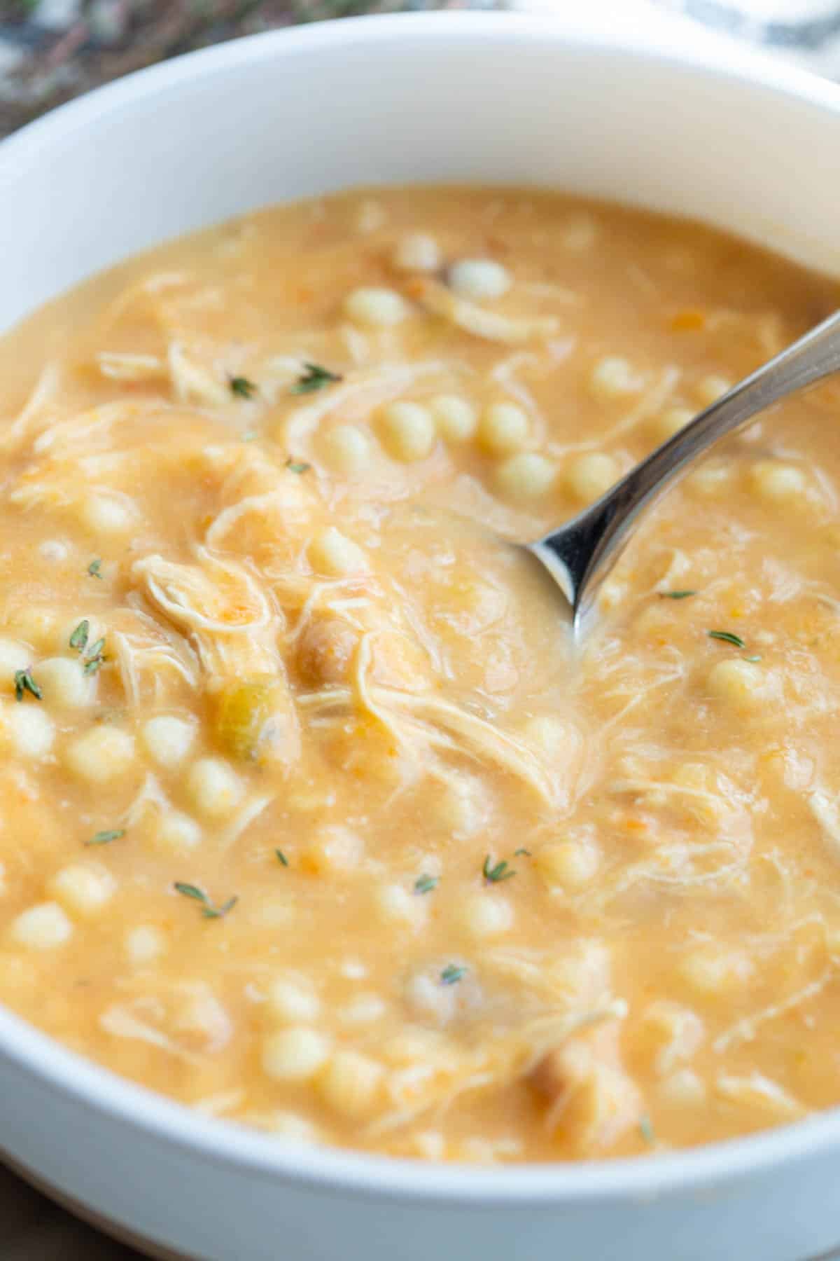 Slow Cooker Italian Penicillin Soup in a shallow bowl with a spoon and fresh thyme sprinkled on top. 