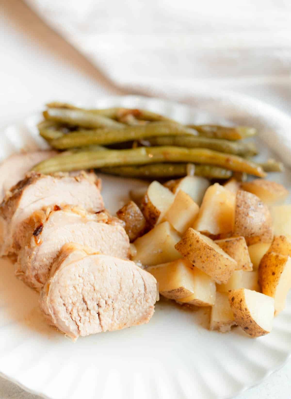 Slow Cooker Pork Tenderloin and Potatoes on a cream colored scalloped plate. 