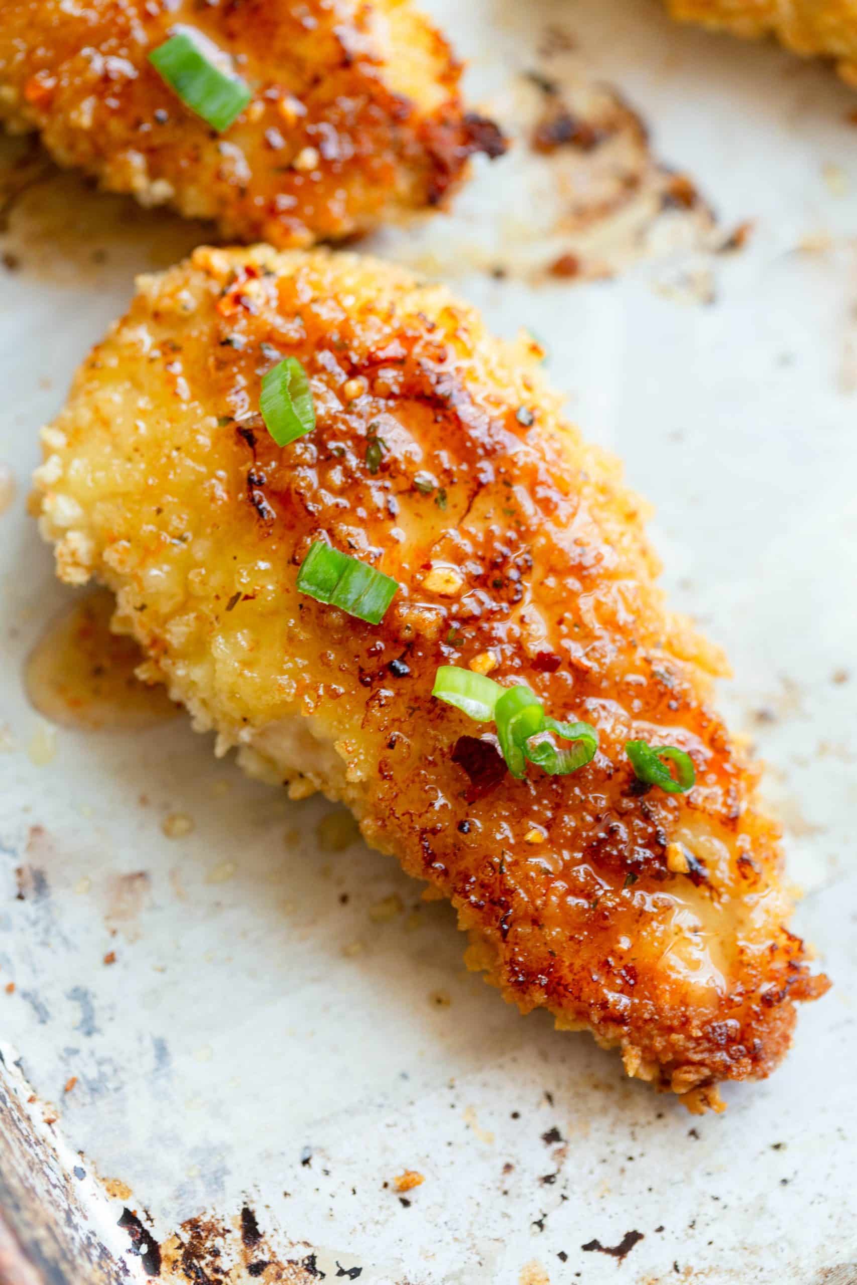 Baked Hot Honey Chicken on a parchment paper lined baking sheet with diced green onions on top and scattered around. 
