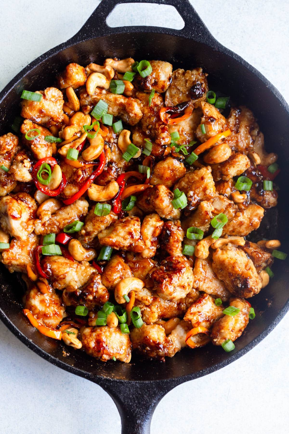 Honey Cashew Chicken topped with green onion in a black cast iron skillet. 
