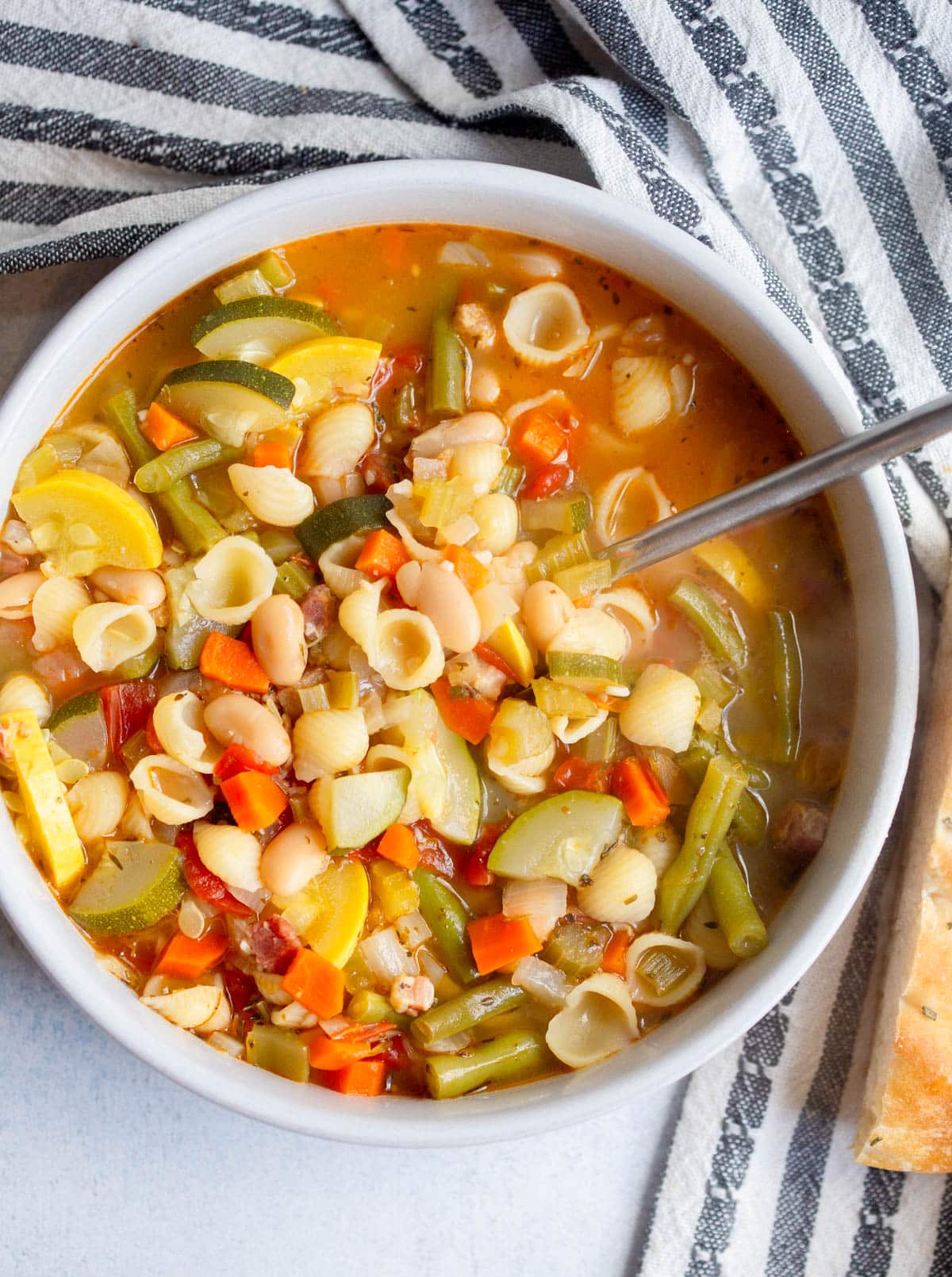 Summer Minestrone in a cream colored bowl with a spoon in it. 