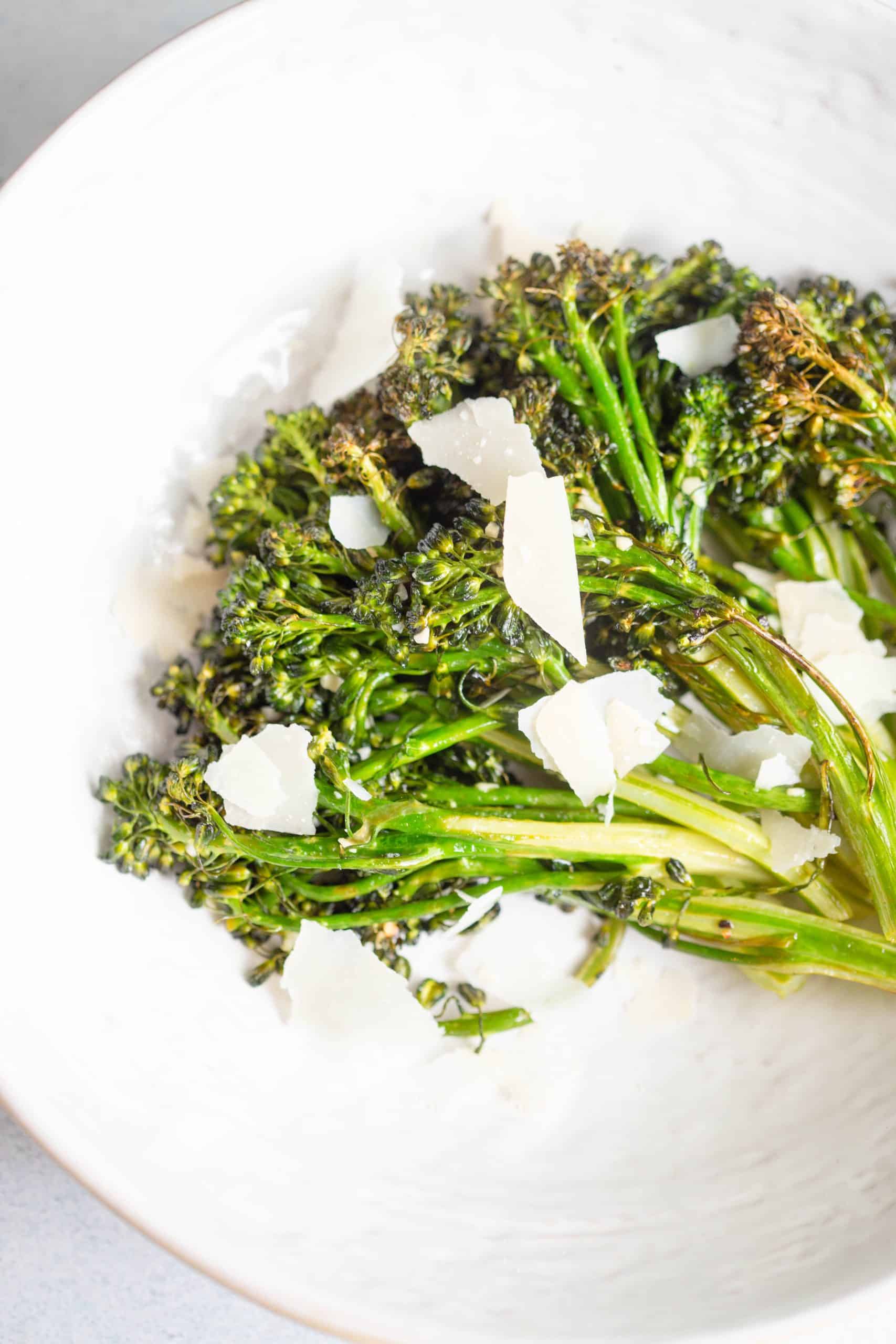 Air Fryer Broccolini in a white bowl topped with shaved Parmesan cheese. 