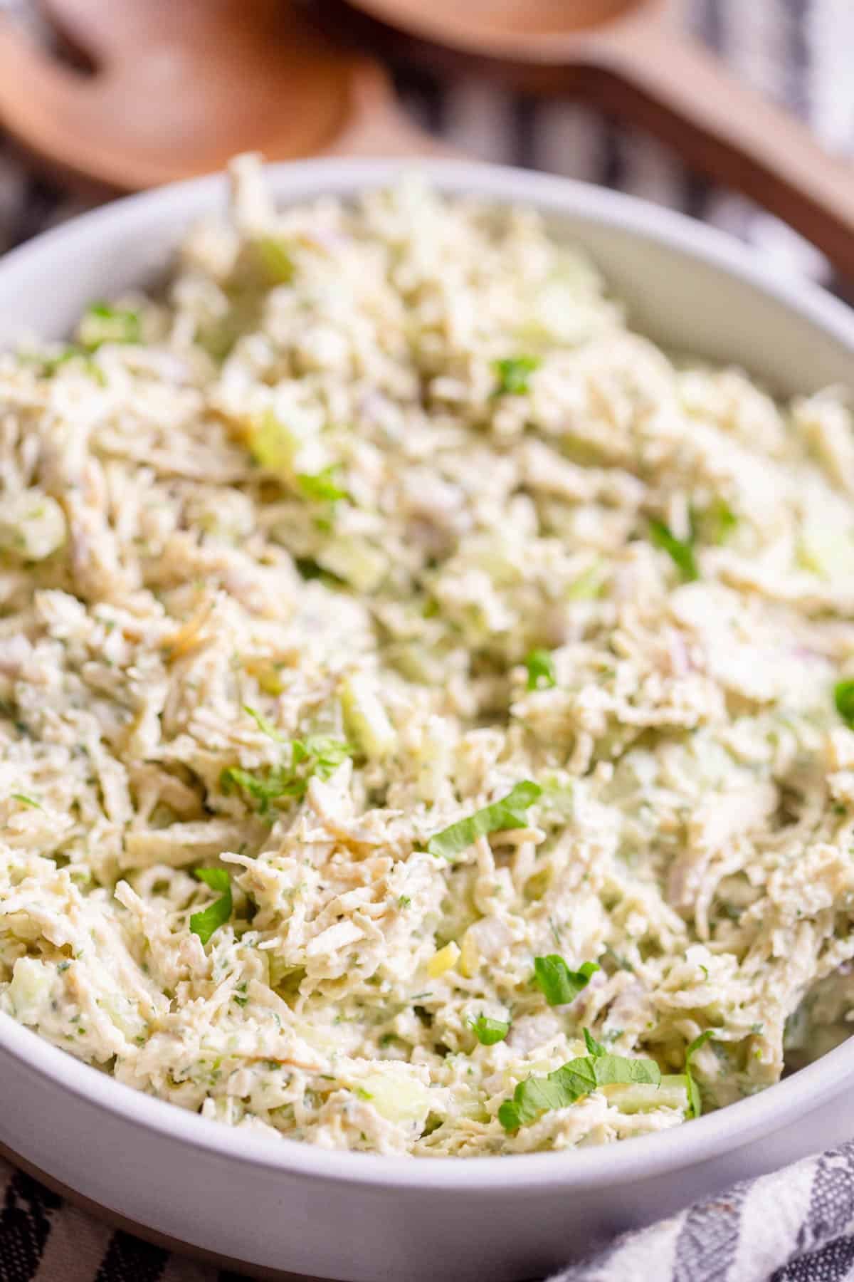 Green Goddess Chicken Salad in a shallow cream colored bowl with a striped towel and wooden salad utensils in the background. 