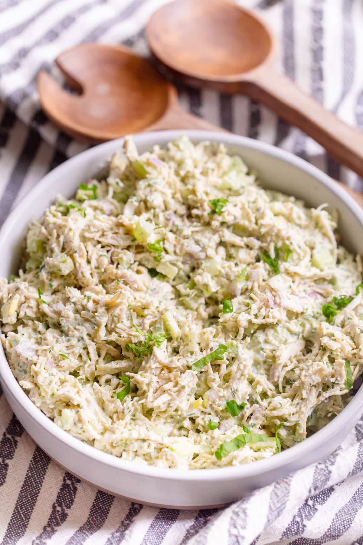 Green Goddess Chicken Salad in a shallow cream colored bowl with a striped towel and wooden salad utensils in the background. 