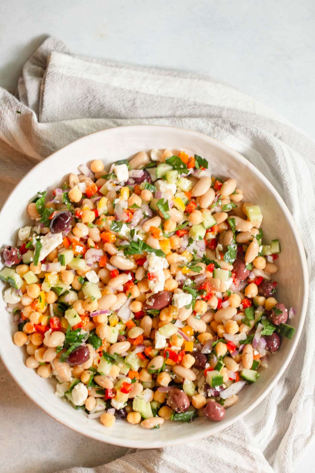 Greek Dense Bean Salad in a cream colored shallow bowl with a neutral colored towel around it.