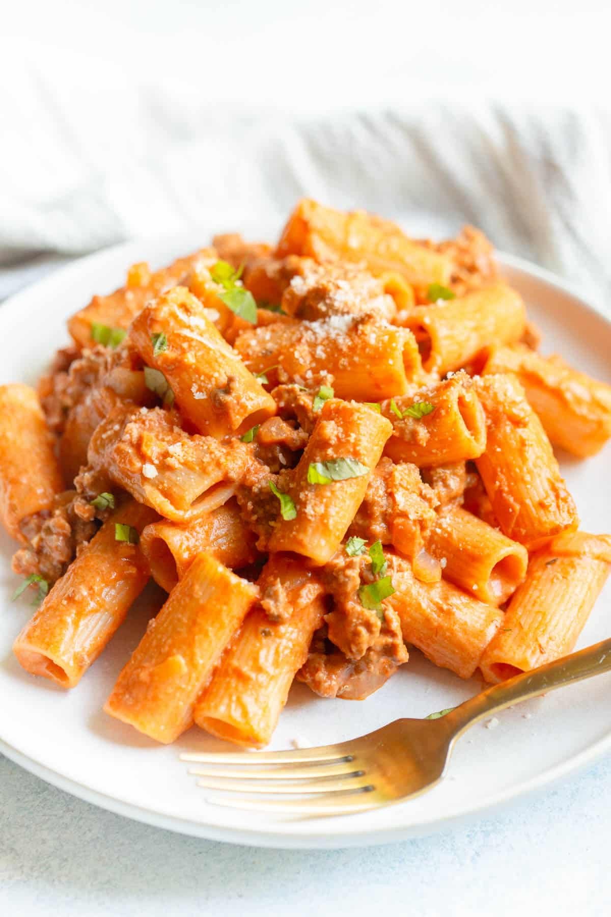 Creamy Italian Sausage Pasta on a white plate sprinkled with grated Parmesan and fresh chopped basil. 