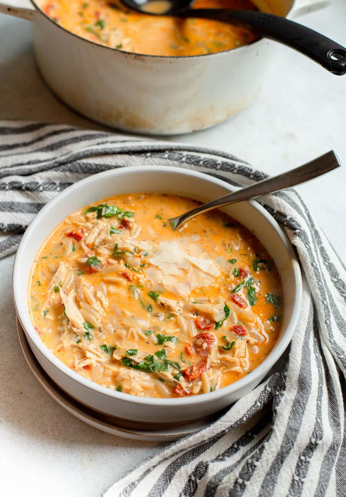 Marry Me Chicken Soup in a cream colored bowl with a gray and white striped towel next to it. 