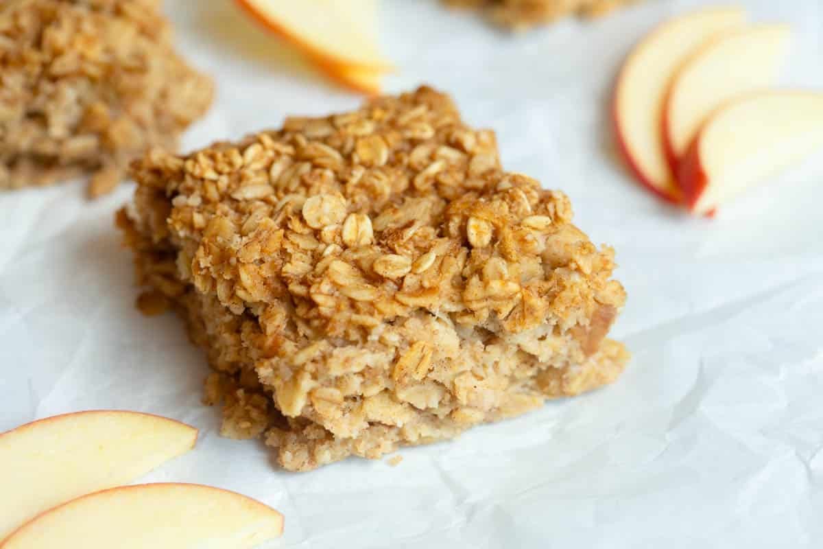 Applesauce Oatmeal Bars on a piece of white parchment paper with apple slices around them. 