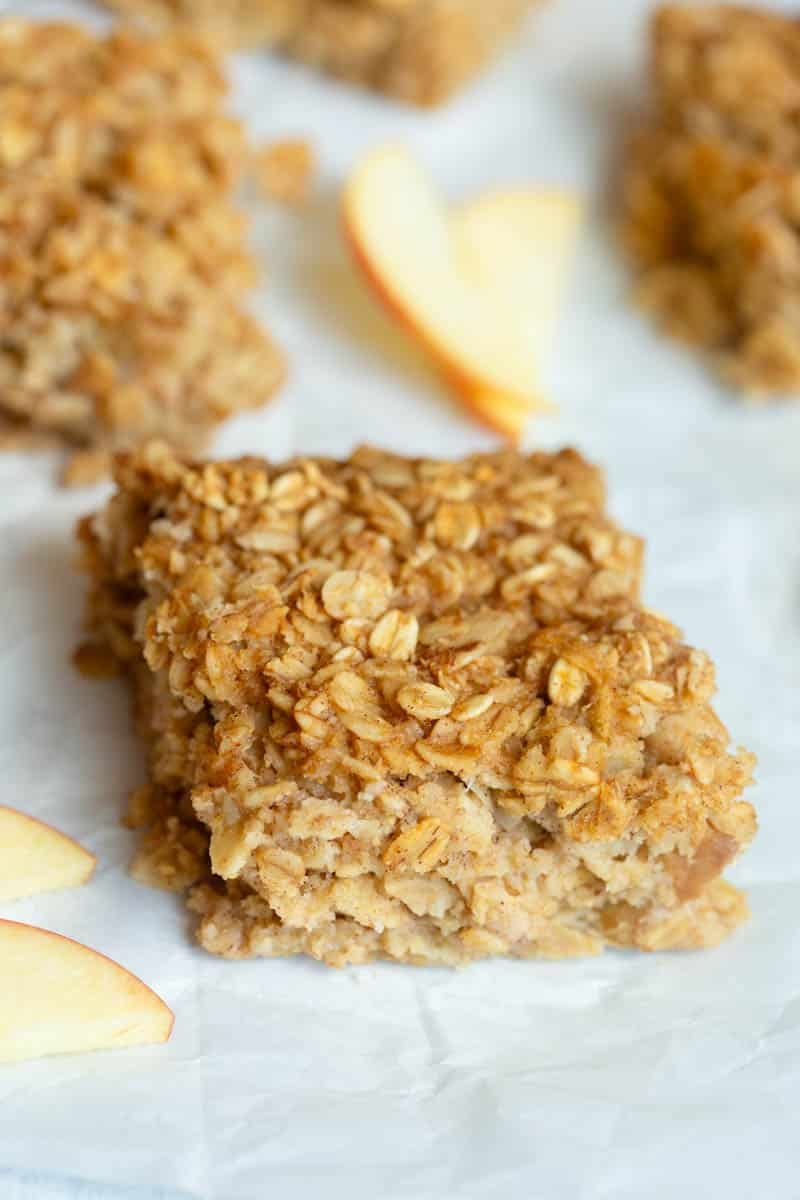 Applesauce Oatmeal Bars on a piece of white parchment paper with apple slices around them. 
