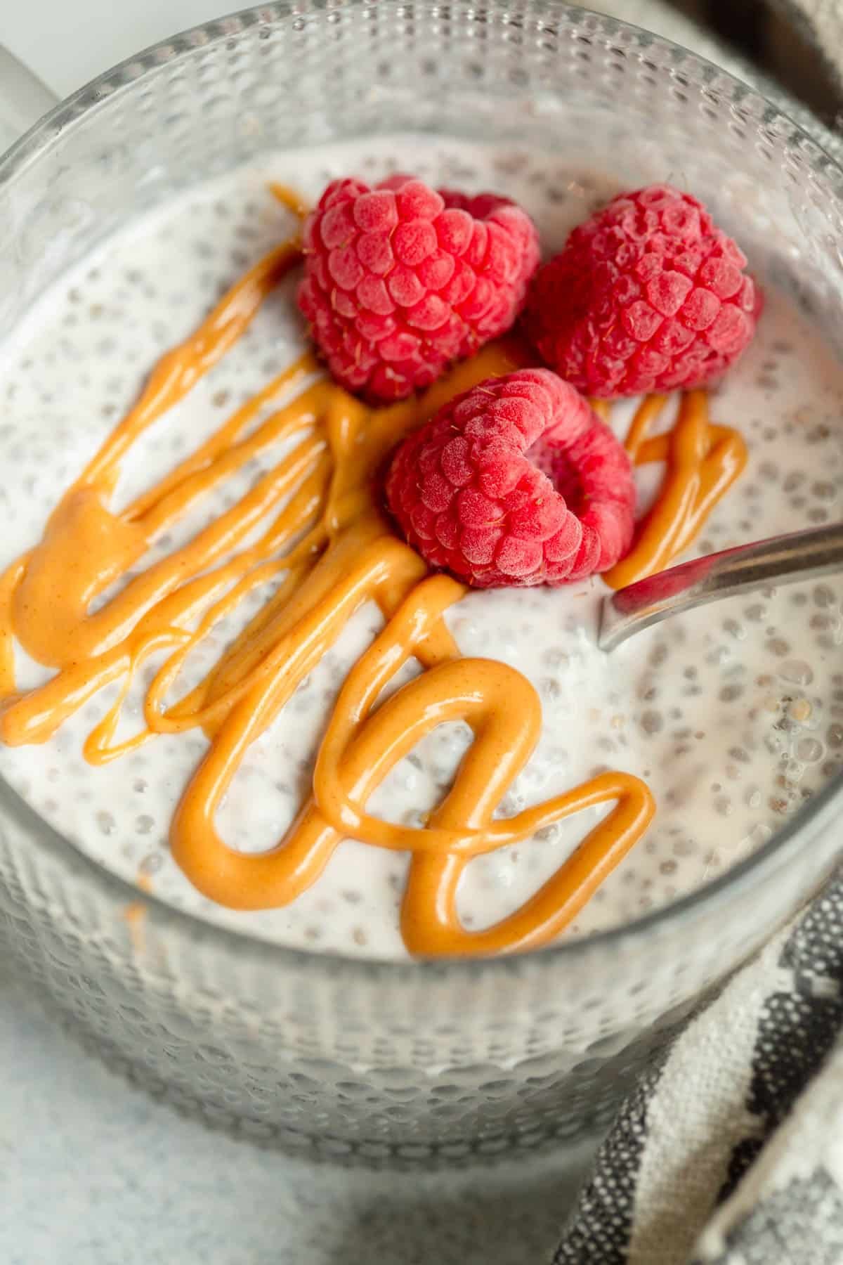 High Protein Chia Seed Pudding drizzled with peanut butter and topped with raspberries. 