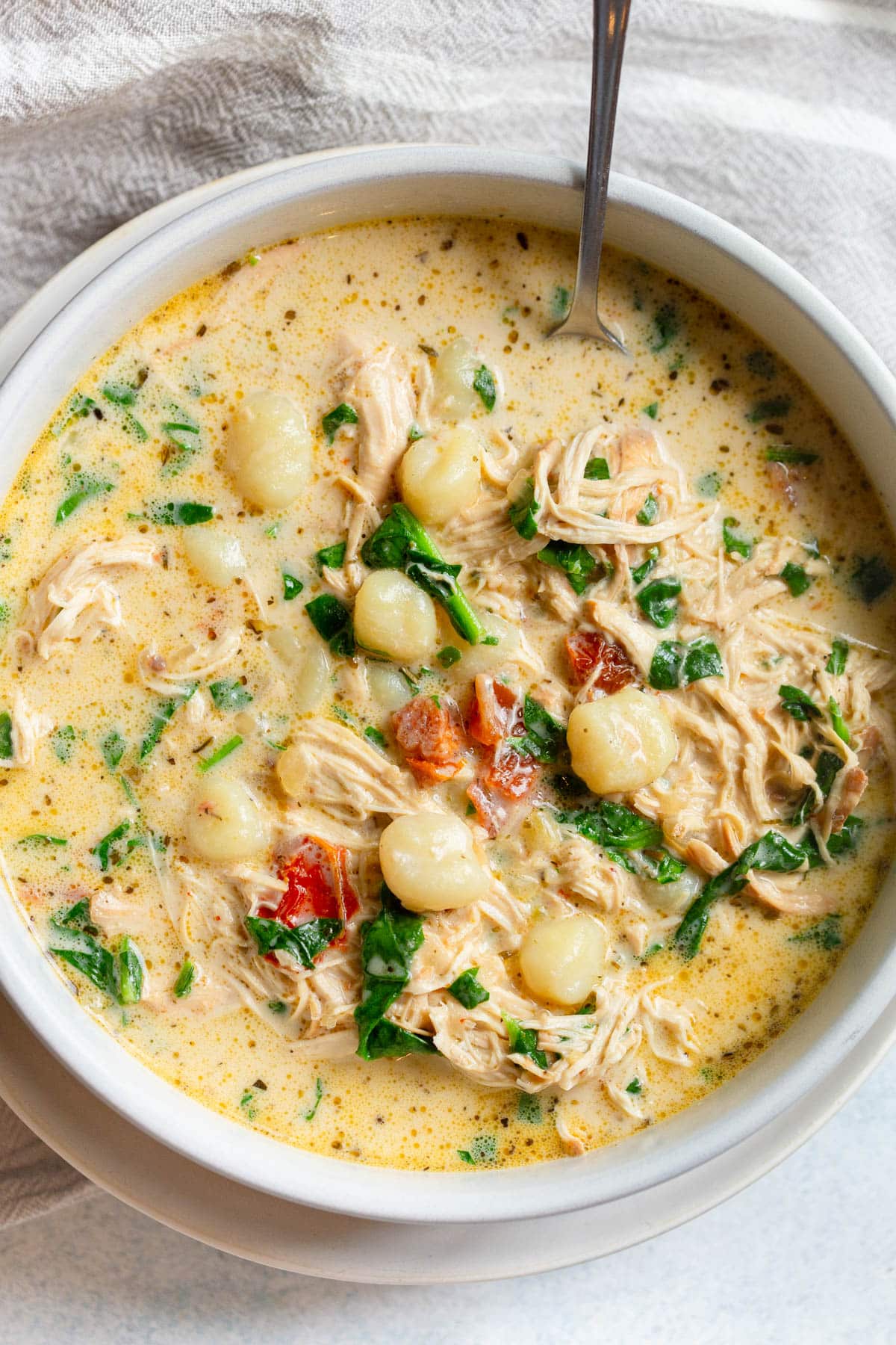 Slow Cooker Tuscan Chicken Gnocchi Soup in a shallow cream colored bowl with a spoon resting in it and a neutral colored napkin next to it. 