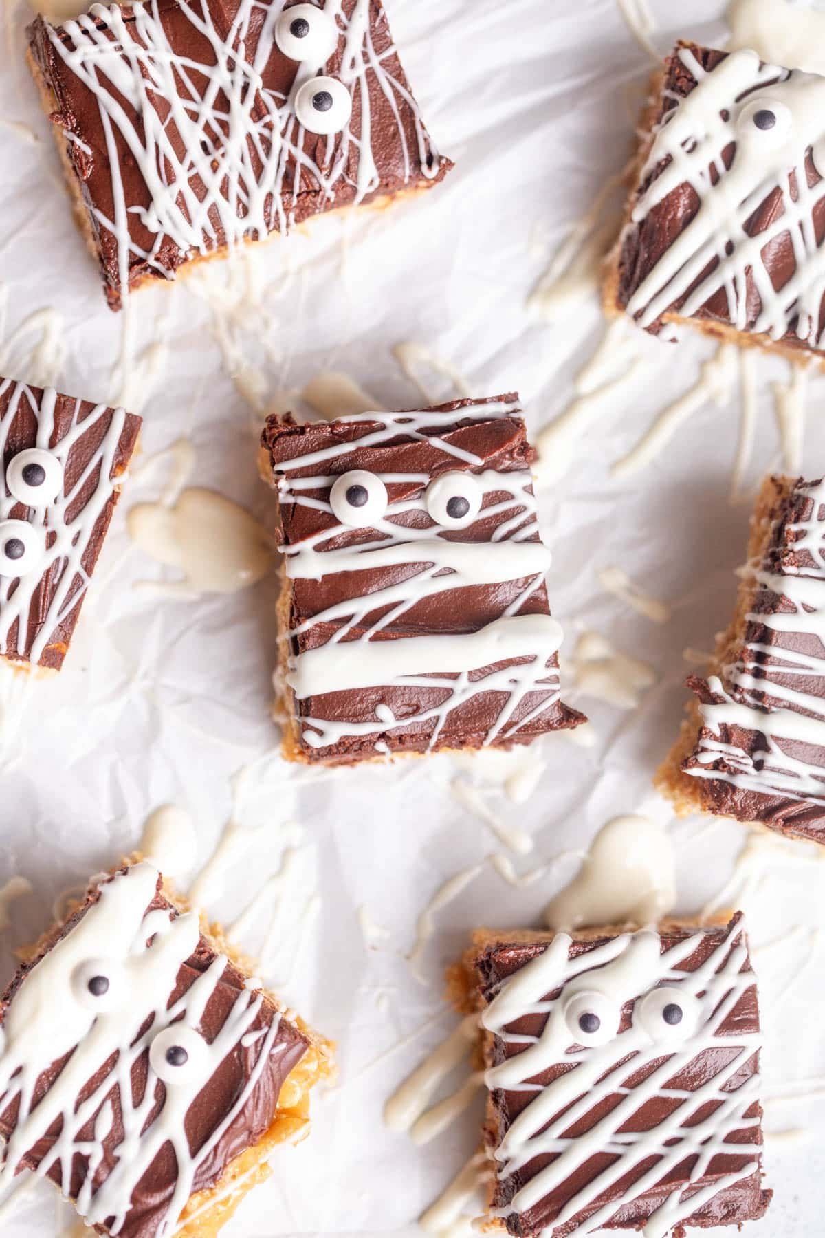 Halloween Scotcharoos drizzled with white chocolate and decorated with edible eyes on a piece of parchment paper.