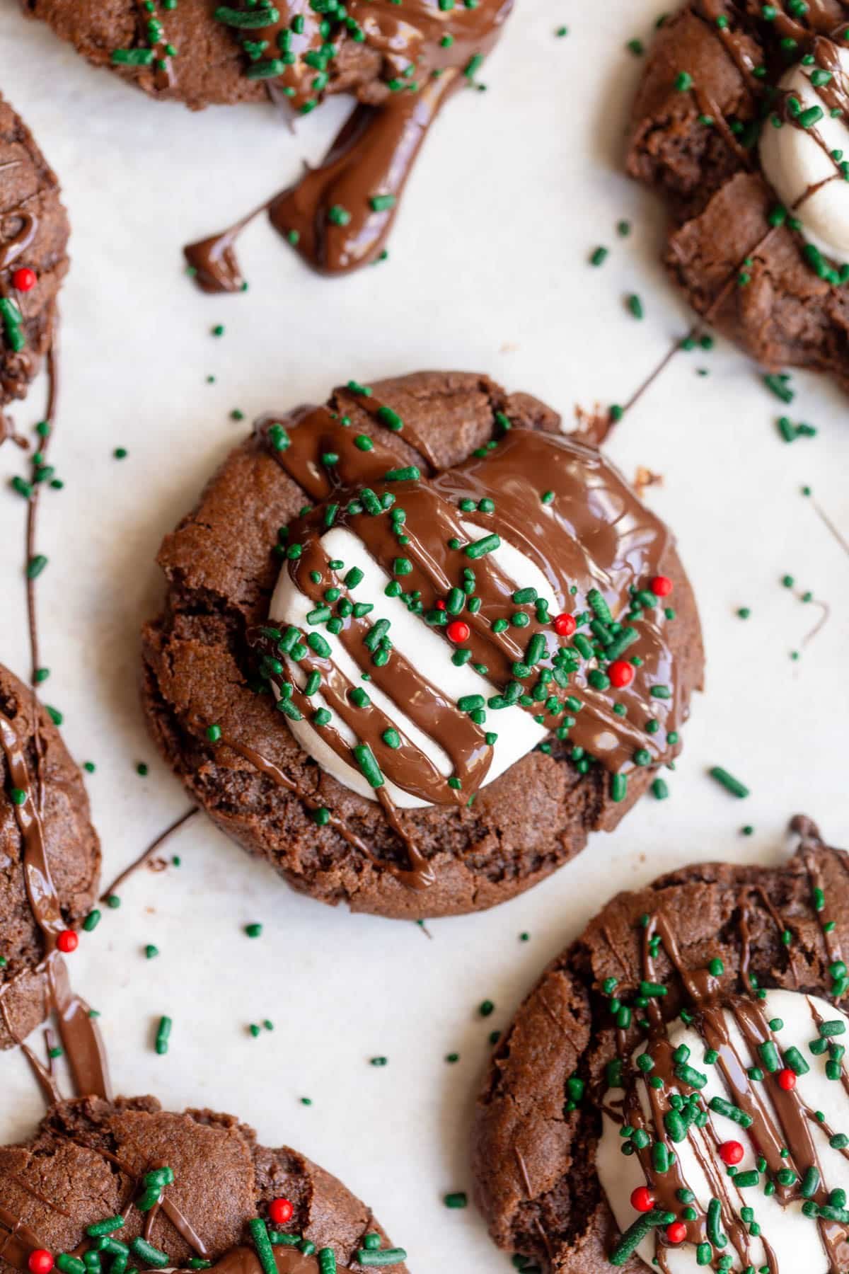 Hot Cocoa cookie on a parchment lined baking sheet, drizzled with chocolate and topped with Christmas colored sprinkles. 