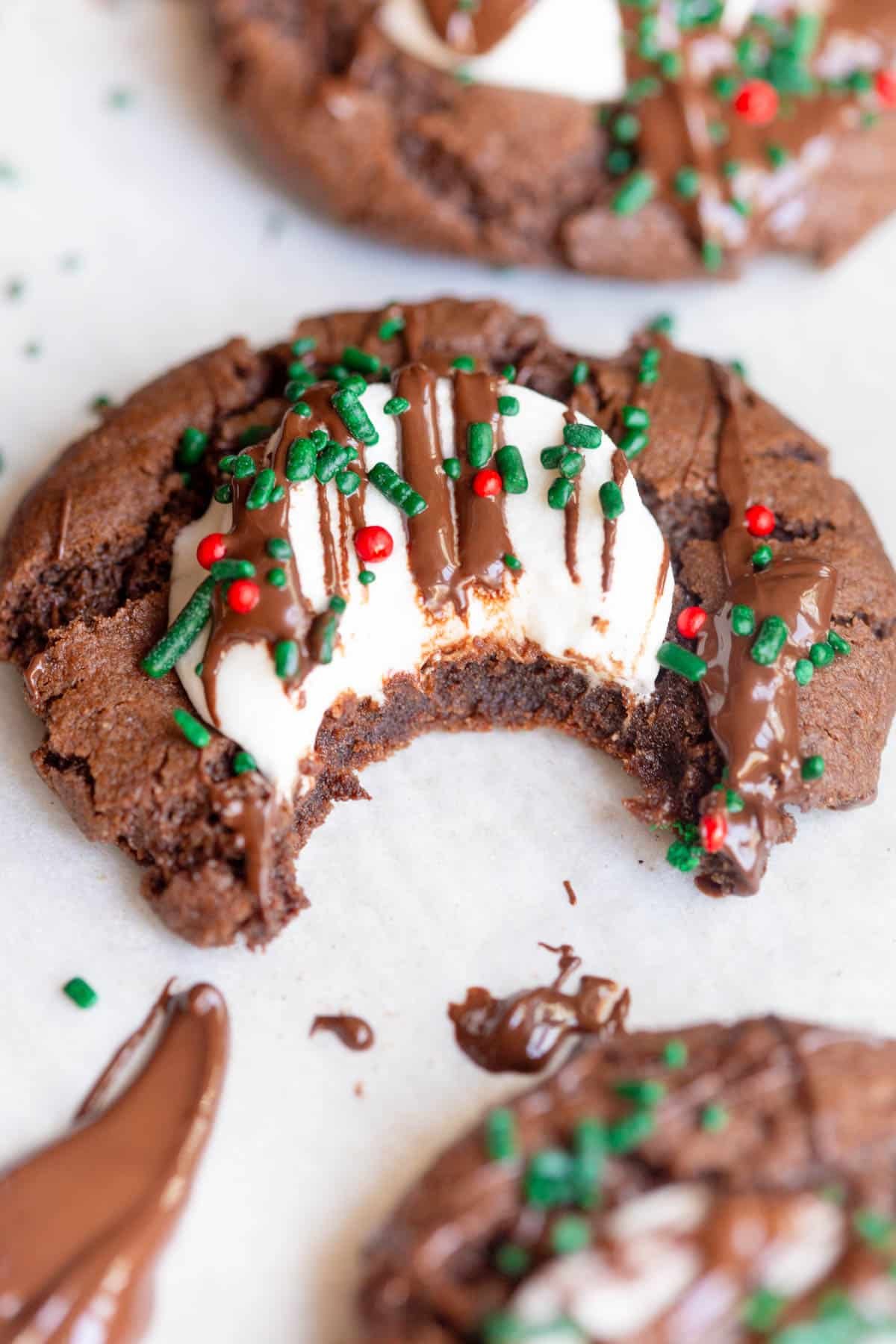 Hot Cocoa cookie on a parchment lined baking sheet, drizzled with chocolate and topped with Christmas colored sprinkles. 