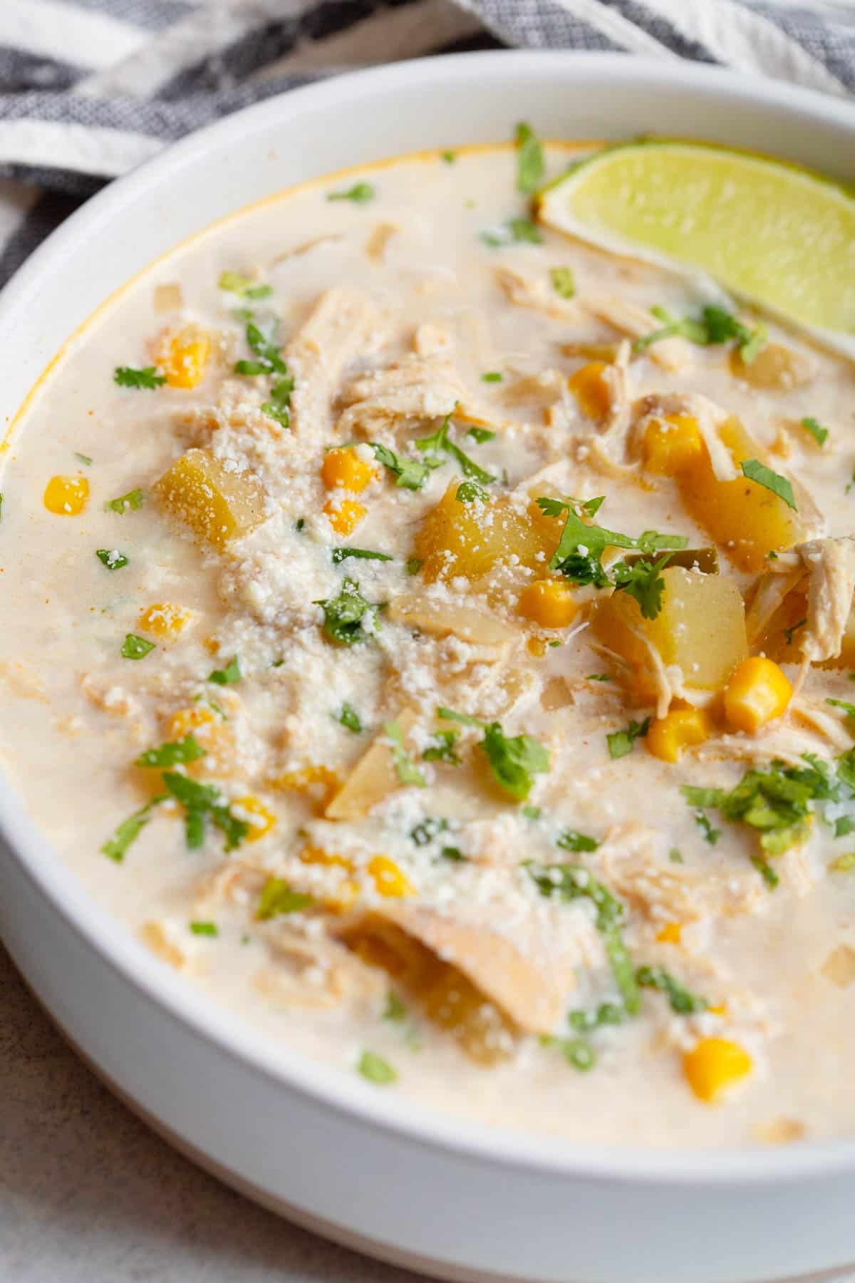 Slow Cooker Mexican Street Corn Soup in a cream colored bowl, topped with fresh chopped cilantro and cotija cheese. 