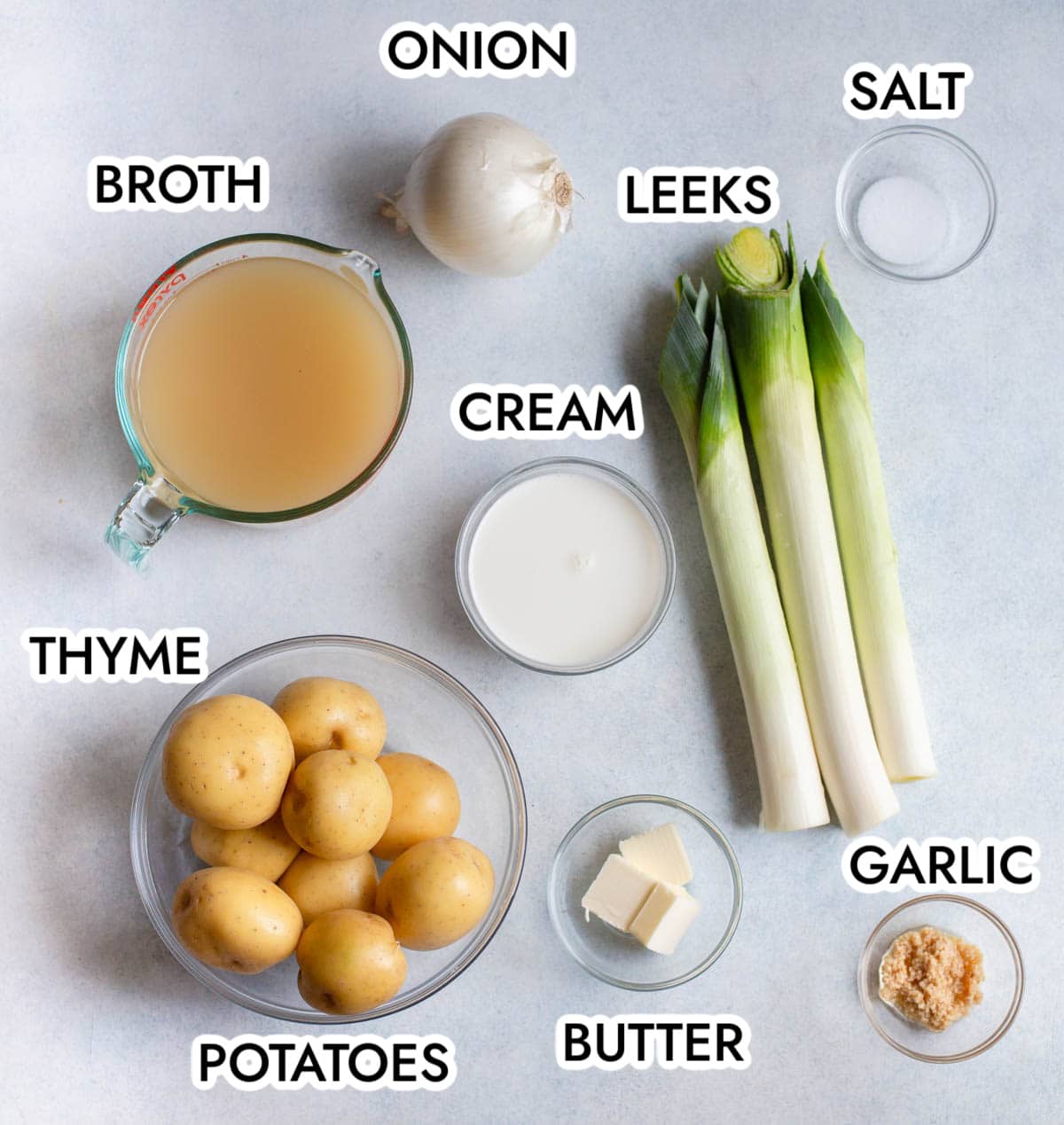 ingredients in slow cooker potato leek soup on a gray background labeled with black letters. 