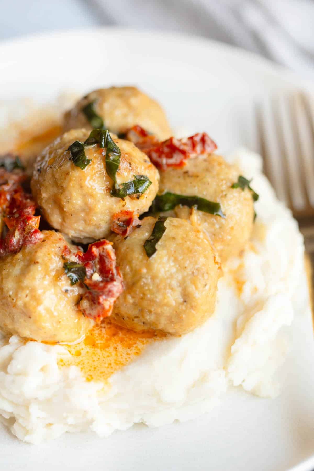 Tuscan Chicken Meatballs on a bed of mashed potatoes topped with fresh basil. 