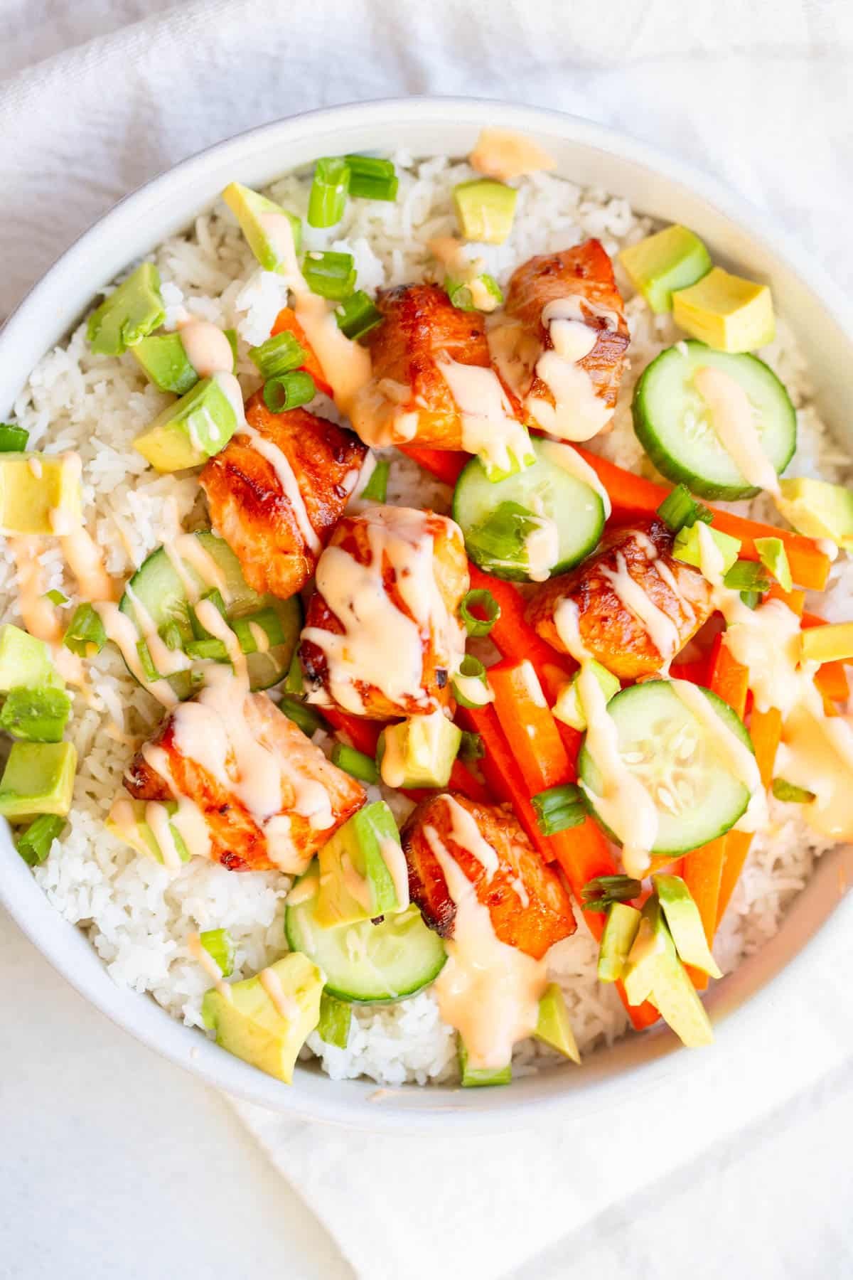 Air Fryer Salmon Bowls in a shallow bowl drizzled with sauce and garnished with green onions. 