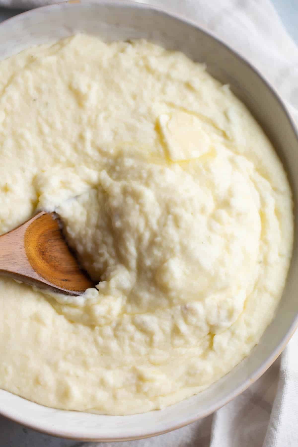 Boursin Mashed Potatoes in a cream colored bowl with a wooden spoon in them. 