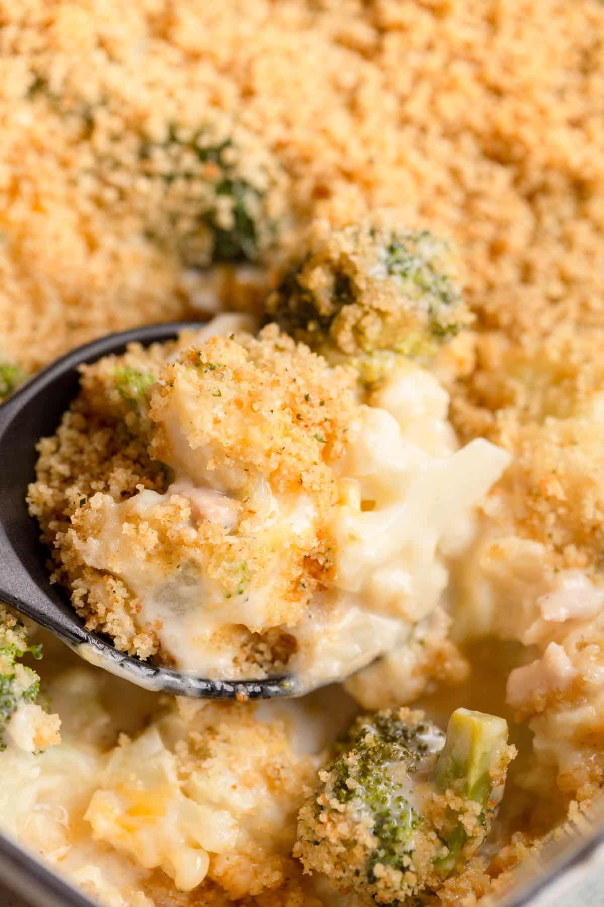 A serving spoon with a scoop of Cheesy Broccoli Cauliflower Casserole.