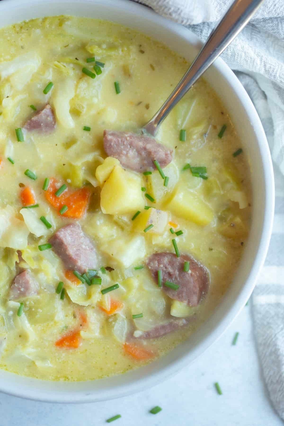 Kielbasa Cabbage Soup in a white bowl with a silver spoon in it. 