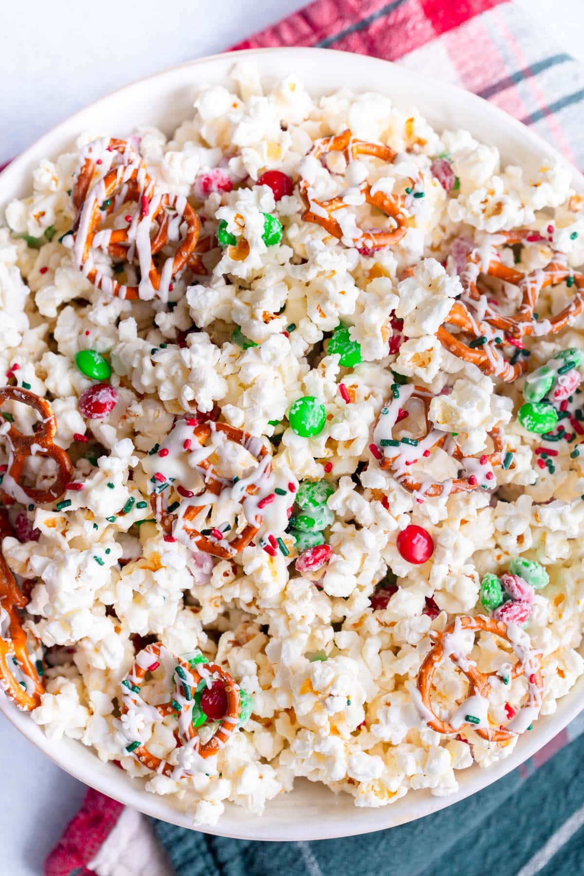 Christmas Popcorn in a white bowl with a red and green towel laying next to it.