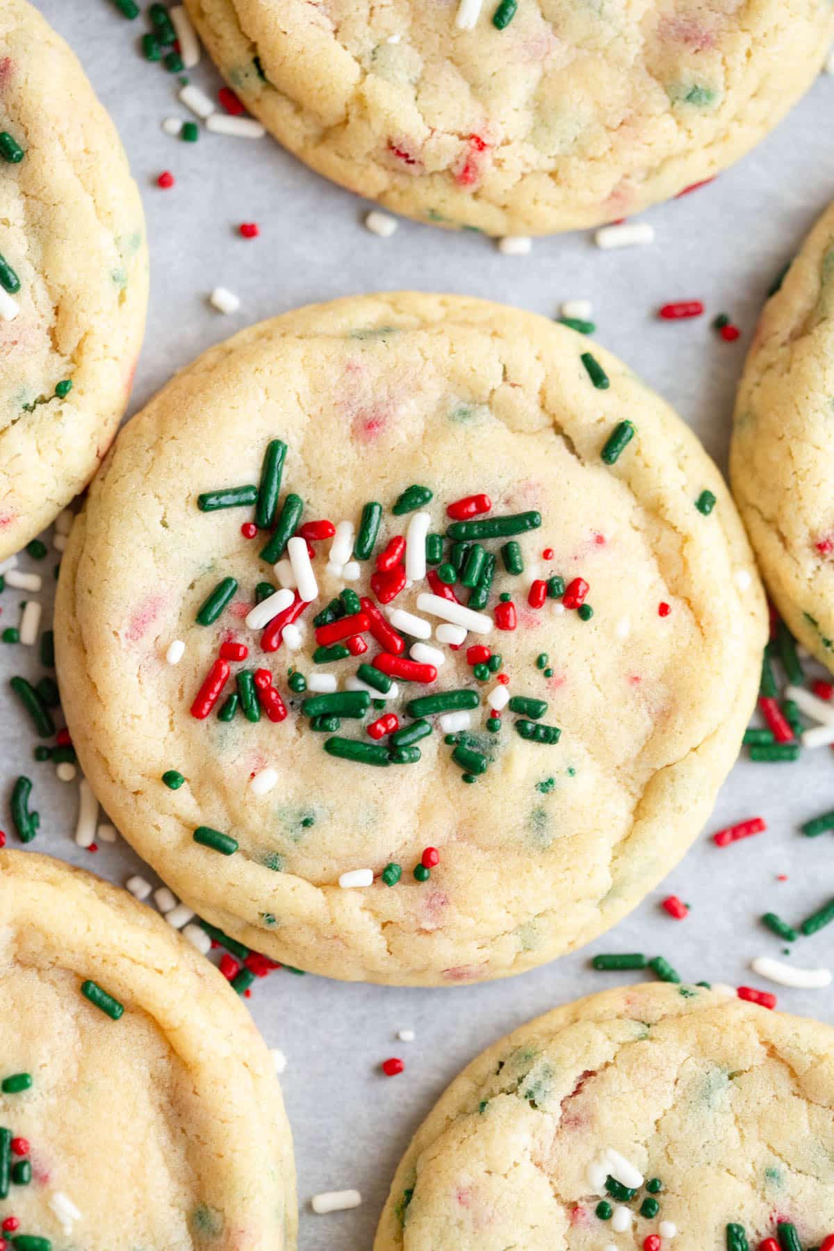 Christmas Sprinkle Sugar Cookies on a baking sheet lined with parchment paper and additional sprinkles scattered around them. 