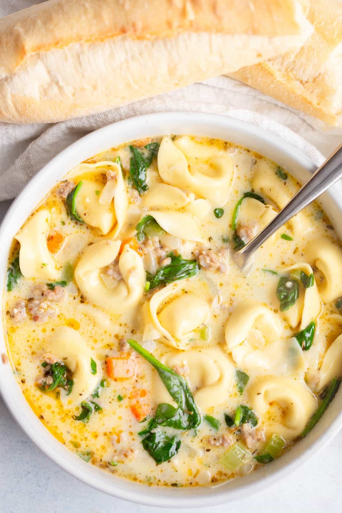 Creamy Tortellini Sausage Soup in a white bowl with a loaf of bread in the background.