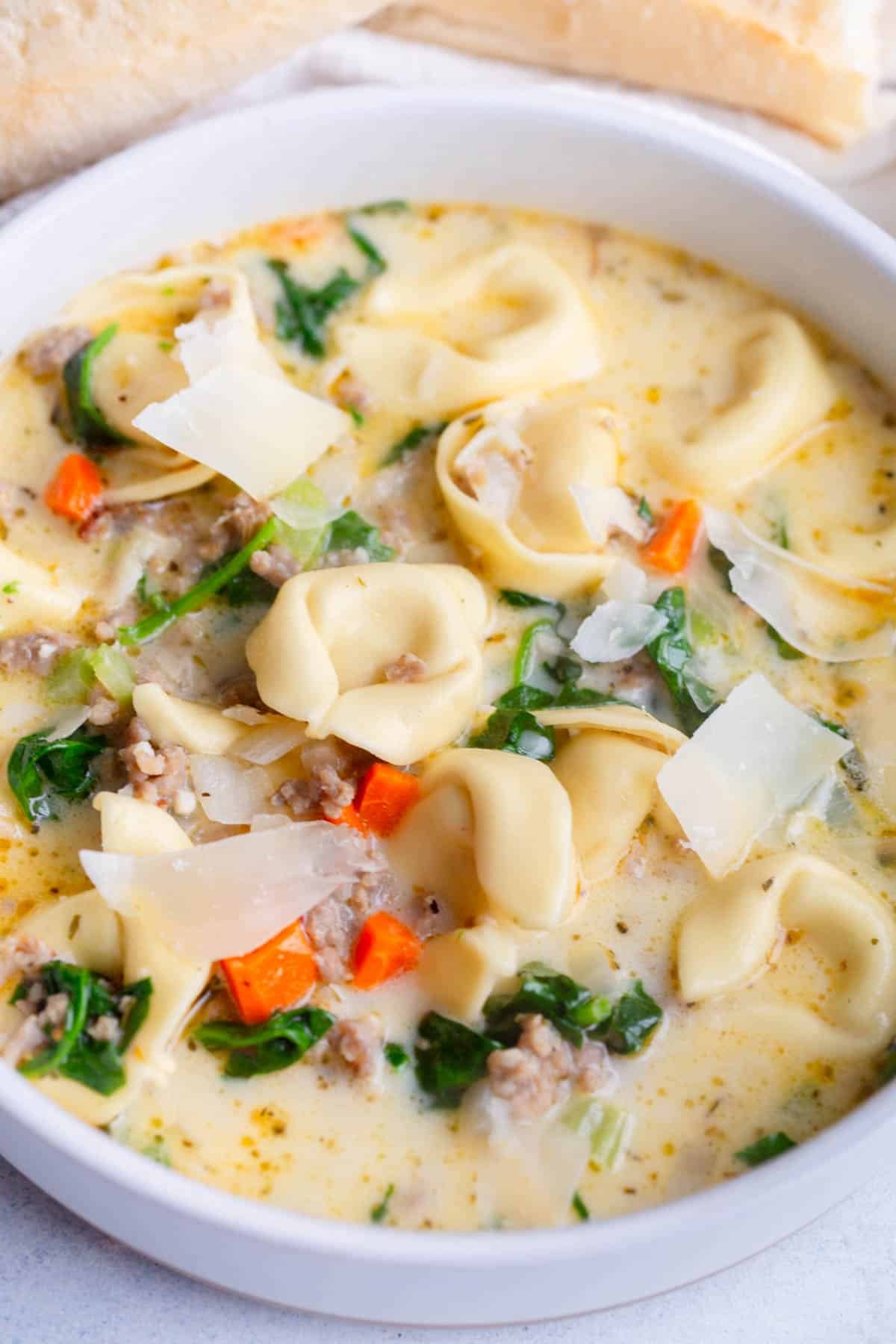 Creamy Tortellini Sausage Soup in a white bowl with a loaf of bread in the background.