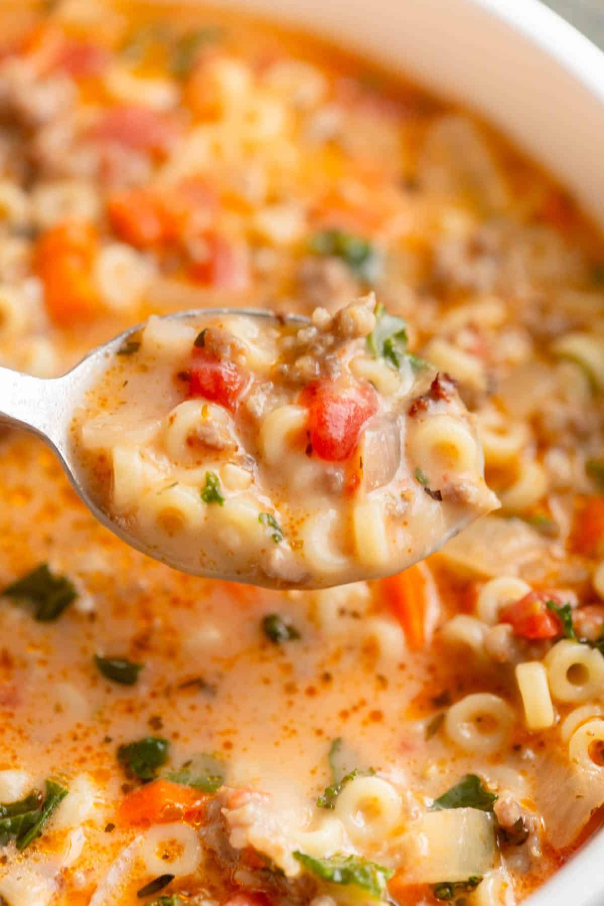 A silver spoon filled with Creamy Italian Sausage Pasta Soup, with the pot of soup in the background. 