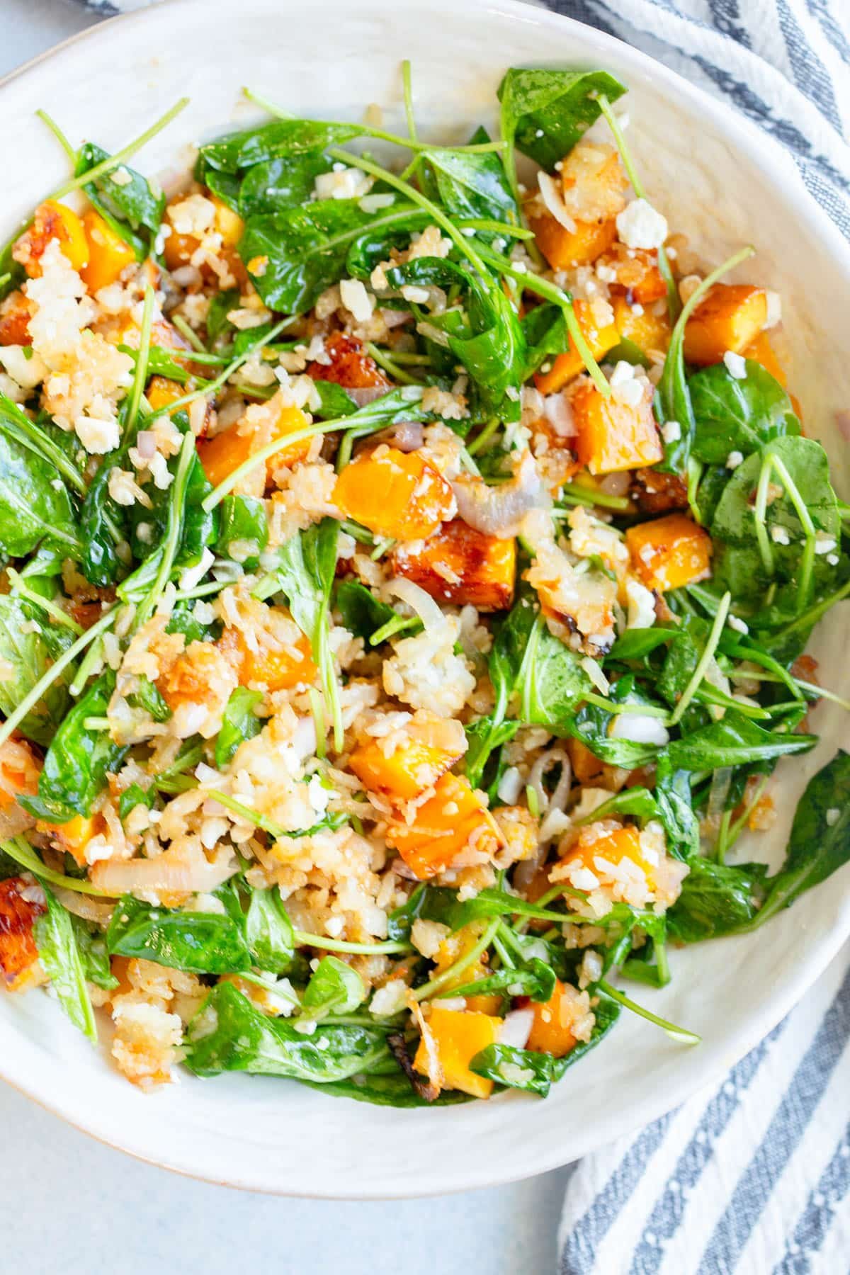 Winter Crispy Rice Salad in a cream colored bowl with a striped napkin next to the bowl.
