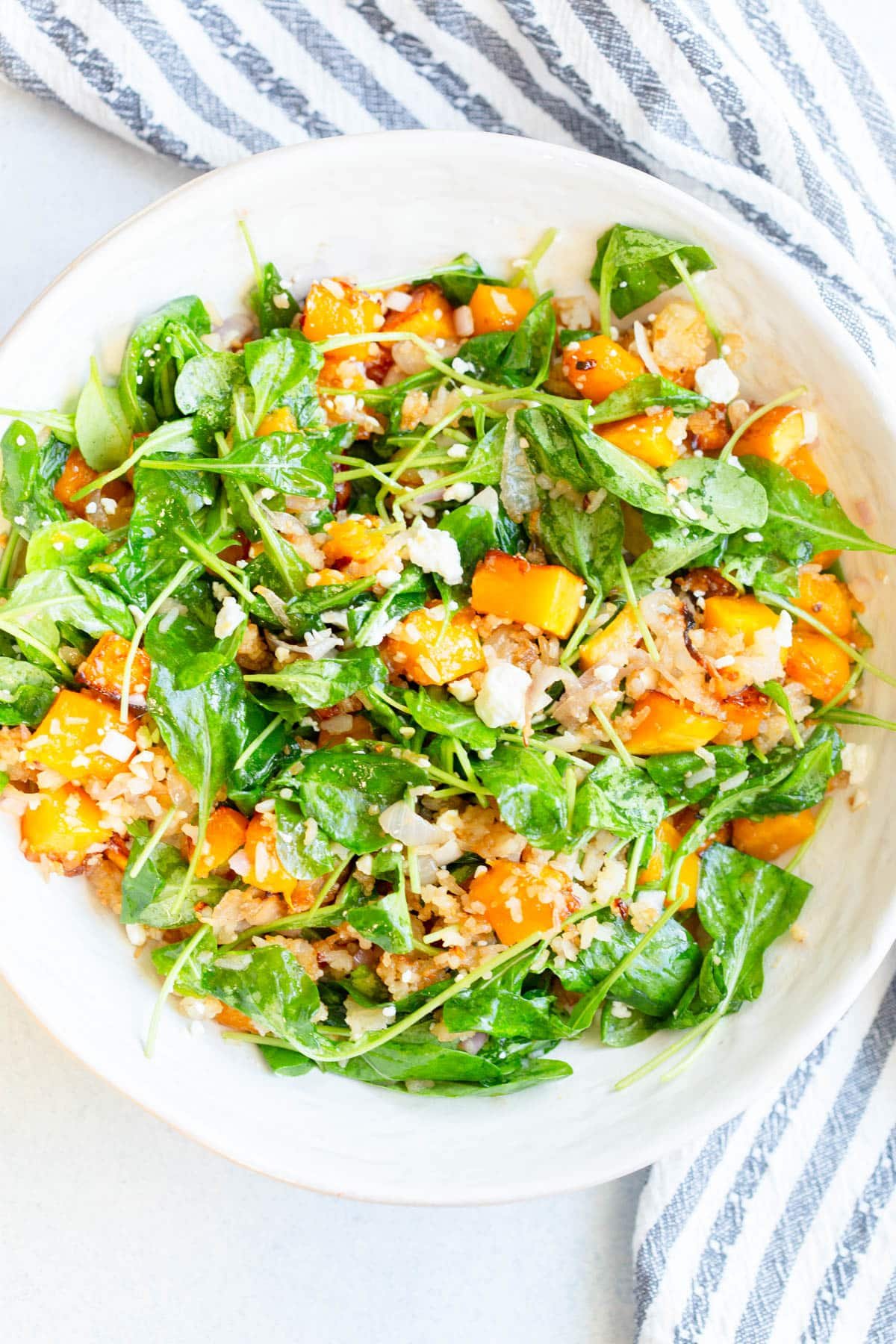 Winter Crispy Rice Salad in a cream colored bowl with a striped napkin next to the bowl.