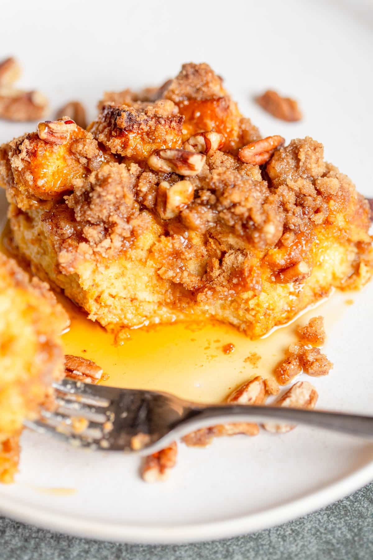 A slice of Brioche Pumpkin French Toast Casserole on a white plate with a forkful taken out of it. 